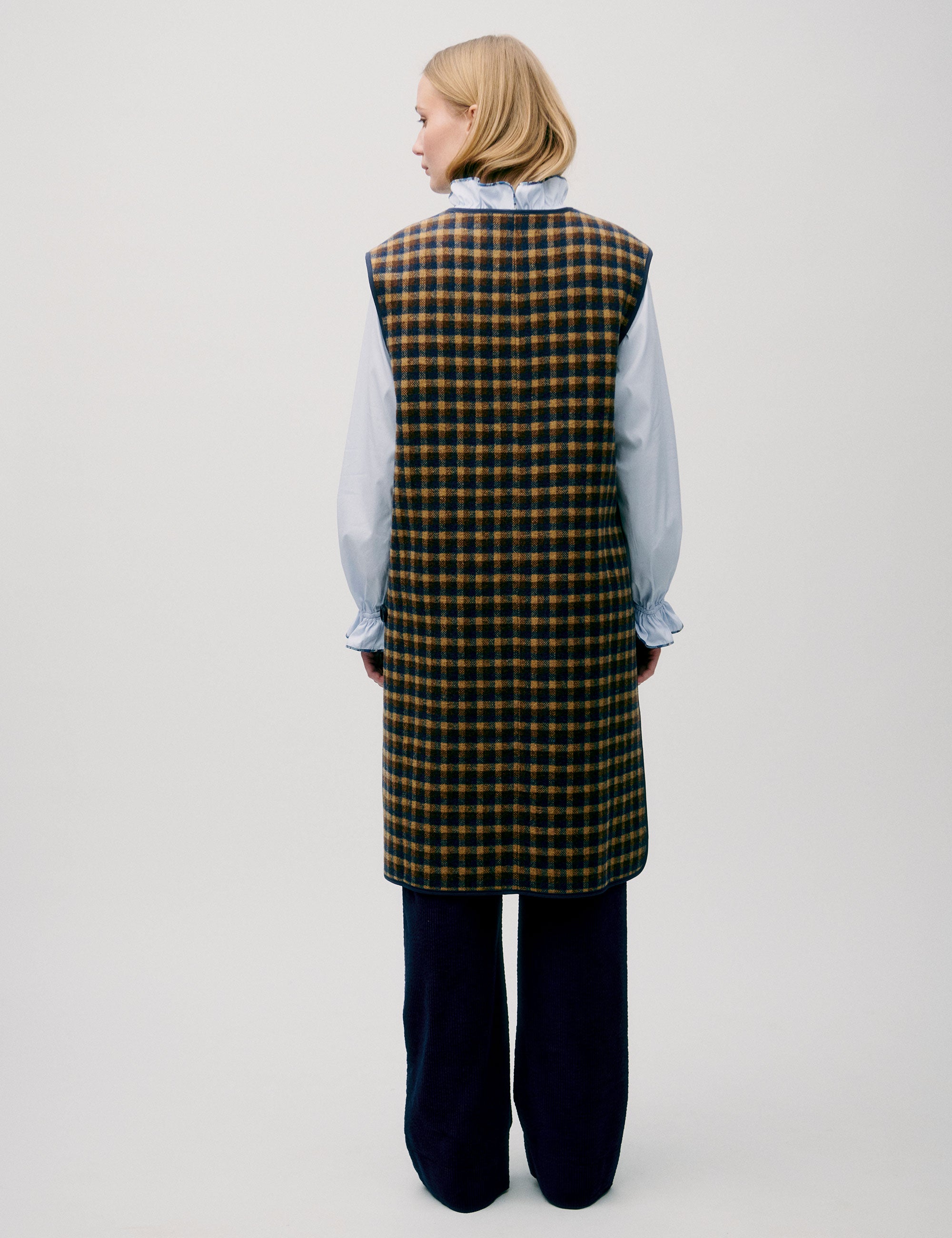 Woman in light blue shirt and long check patterned vest in yellow and black