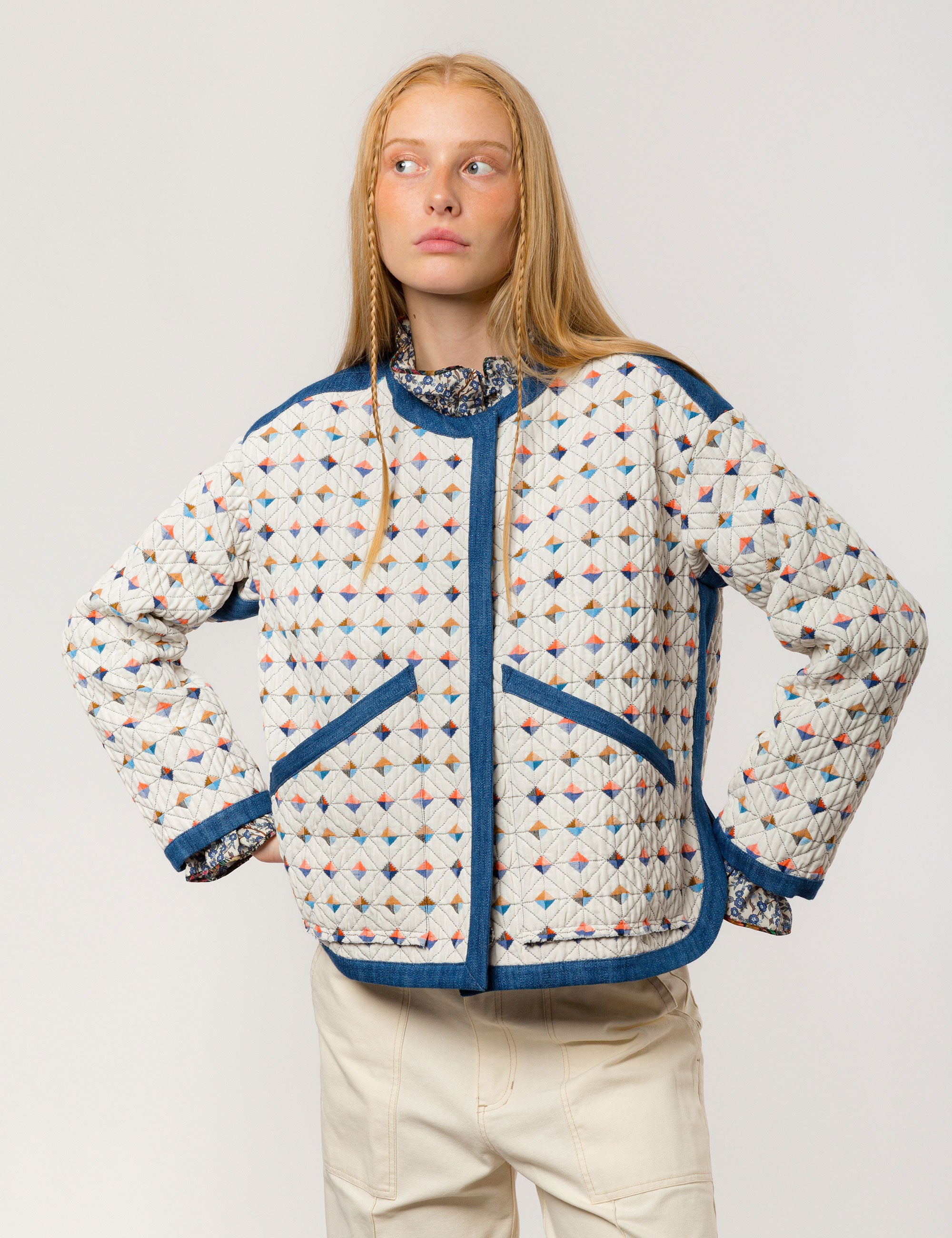 Woman in reversible white quilted jacket with multi-colored check print, blue pipings and pockets and creme colored canvas pants