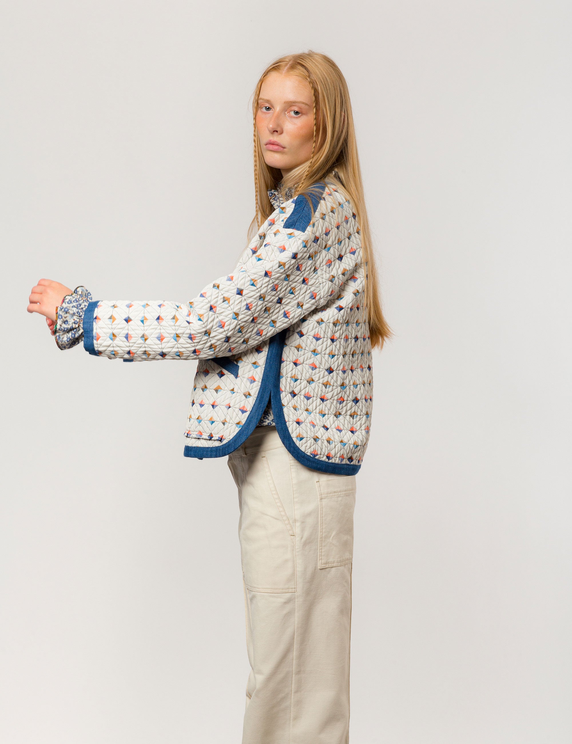 Woman in reversible white quilt jacket with multi-colored check print, blue pipings and pockets, white and blue floral print shirt with frills and creme colored canvas pants