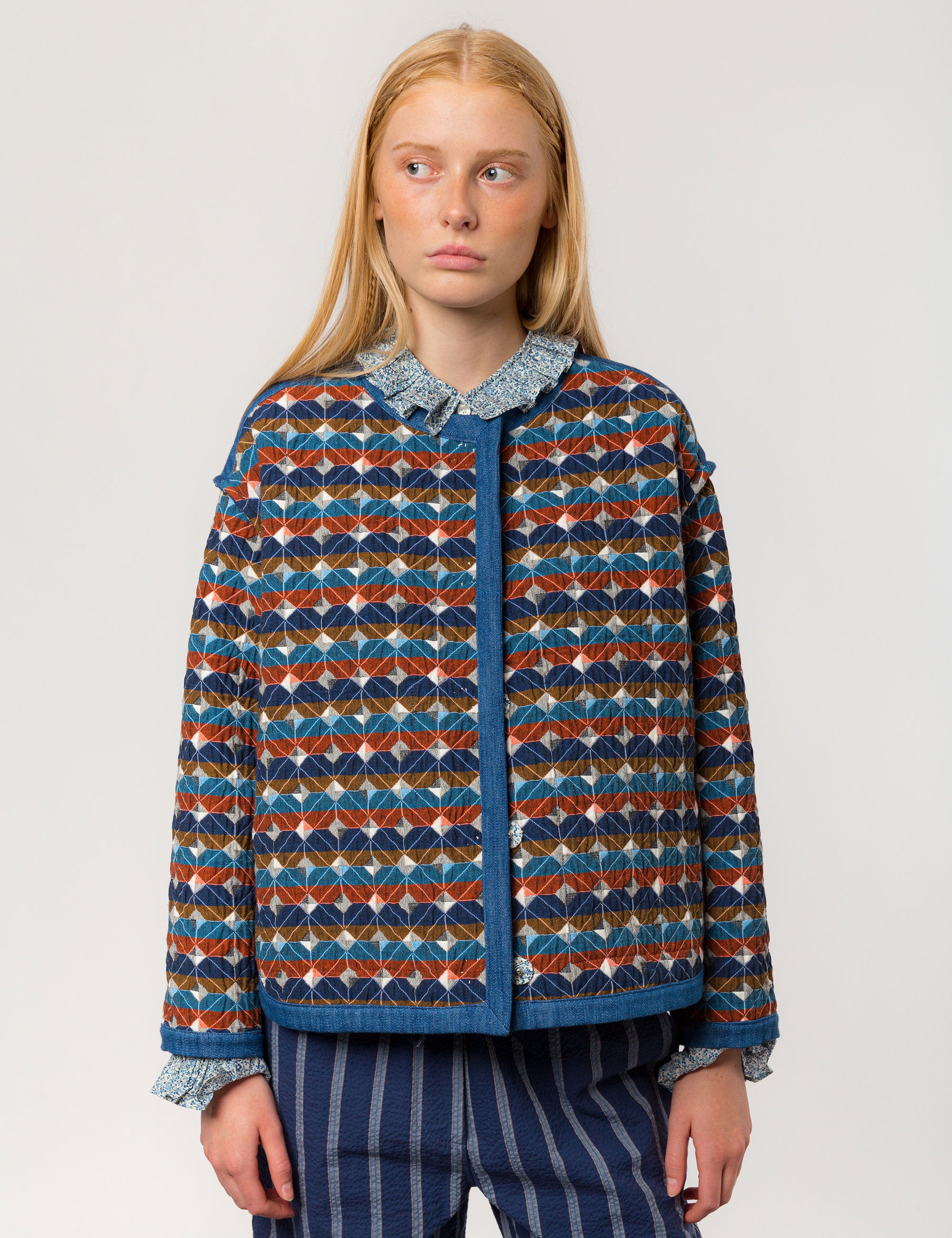 Woman in check print multi-colored quilted women's jacket with long sleeves, buttons and blue pipings and blue and white striped pants