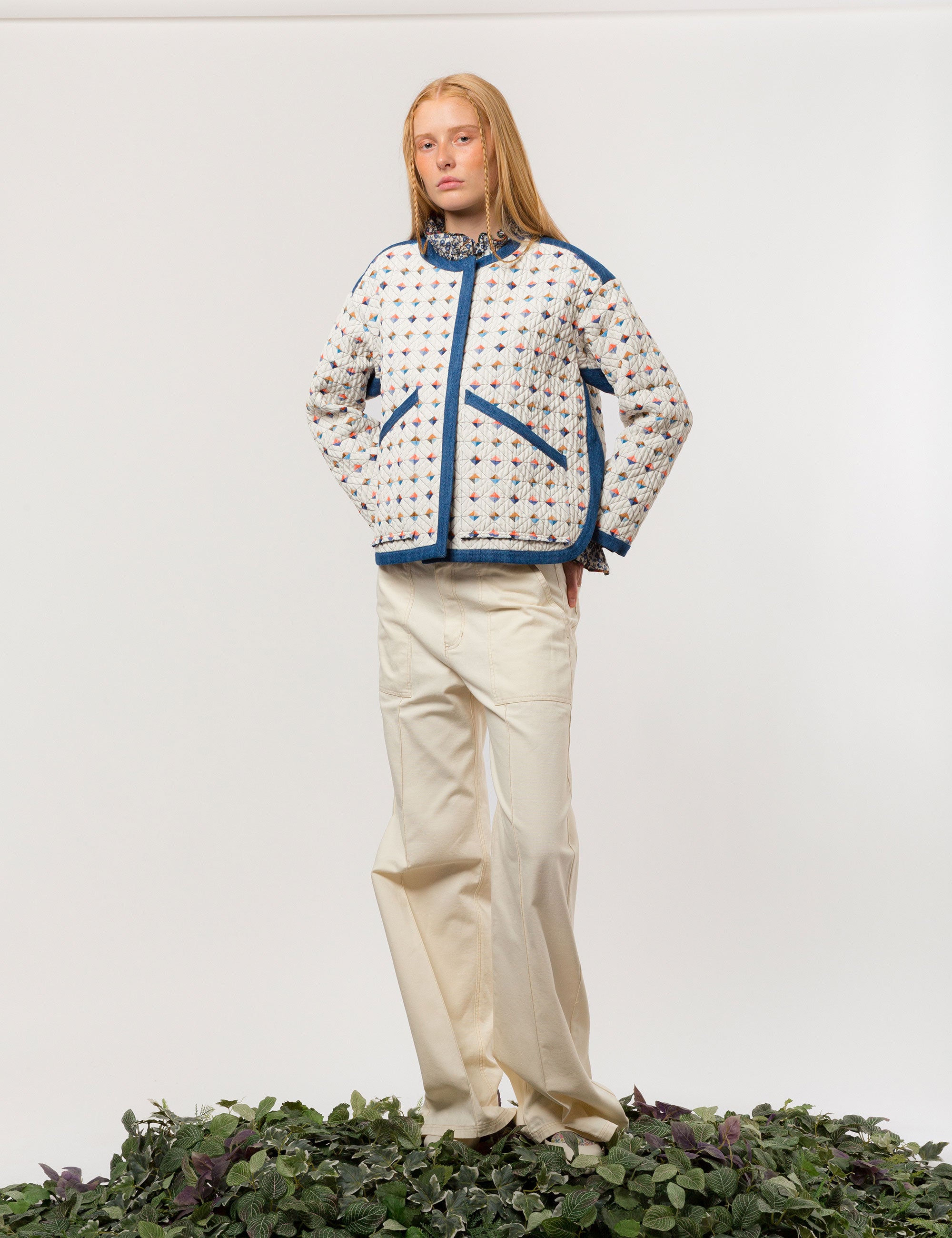 Woman in reversible white quilt jacket with multi-colored check print, blue pipings and pockets, white and blue floral print shirt with frills and creme colored canvas pants