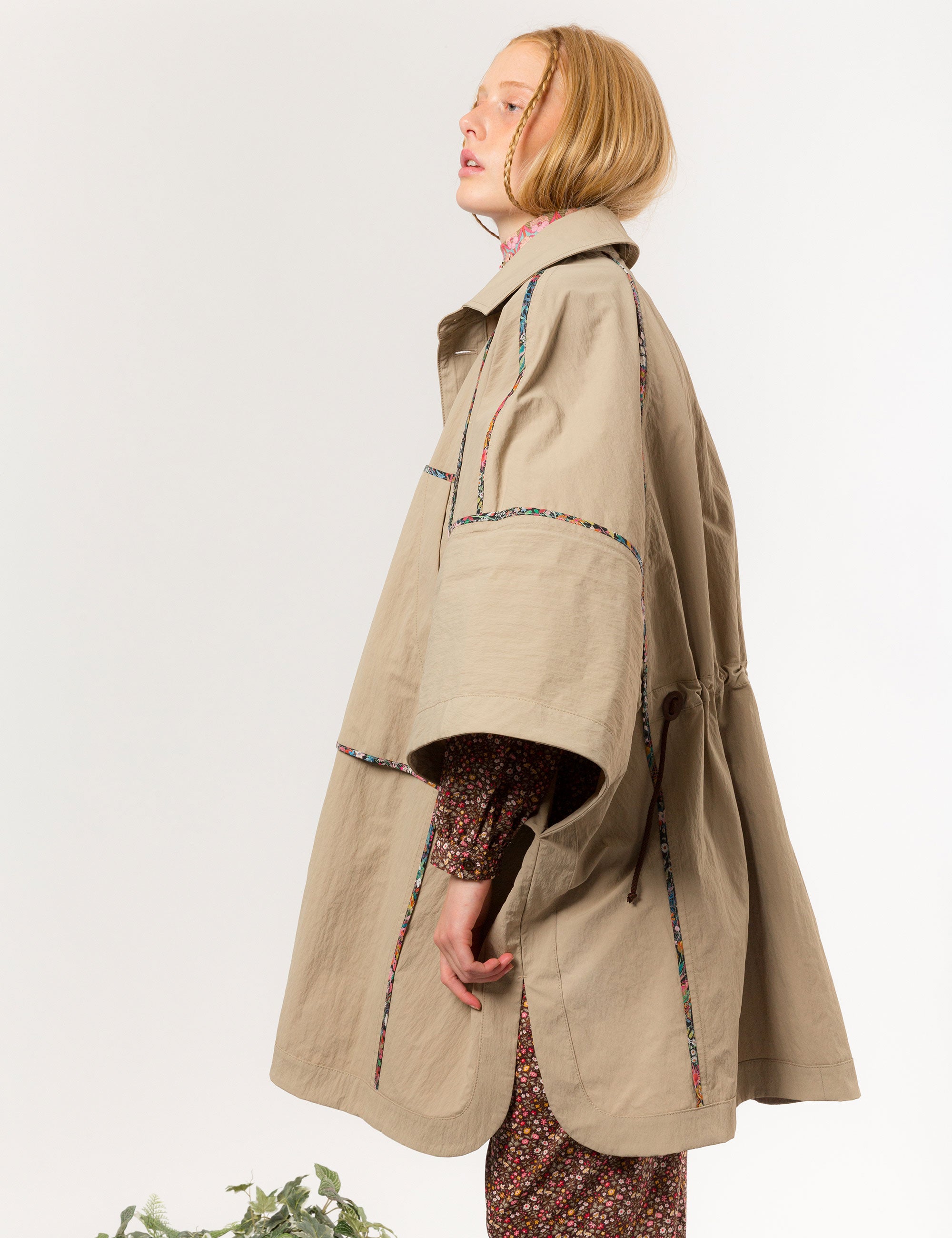 Woman in beige khaki jacket with black buttons, pockets and floral pipings, and brown floral dress