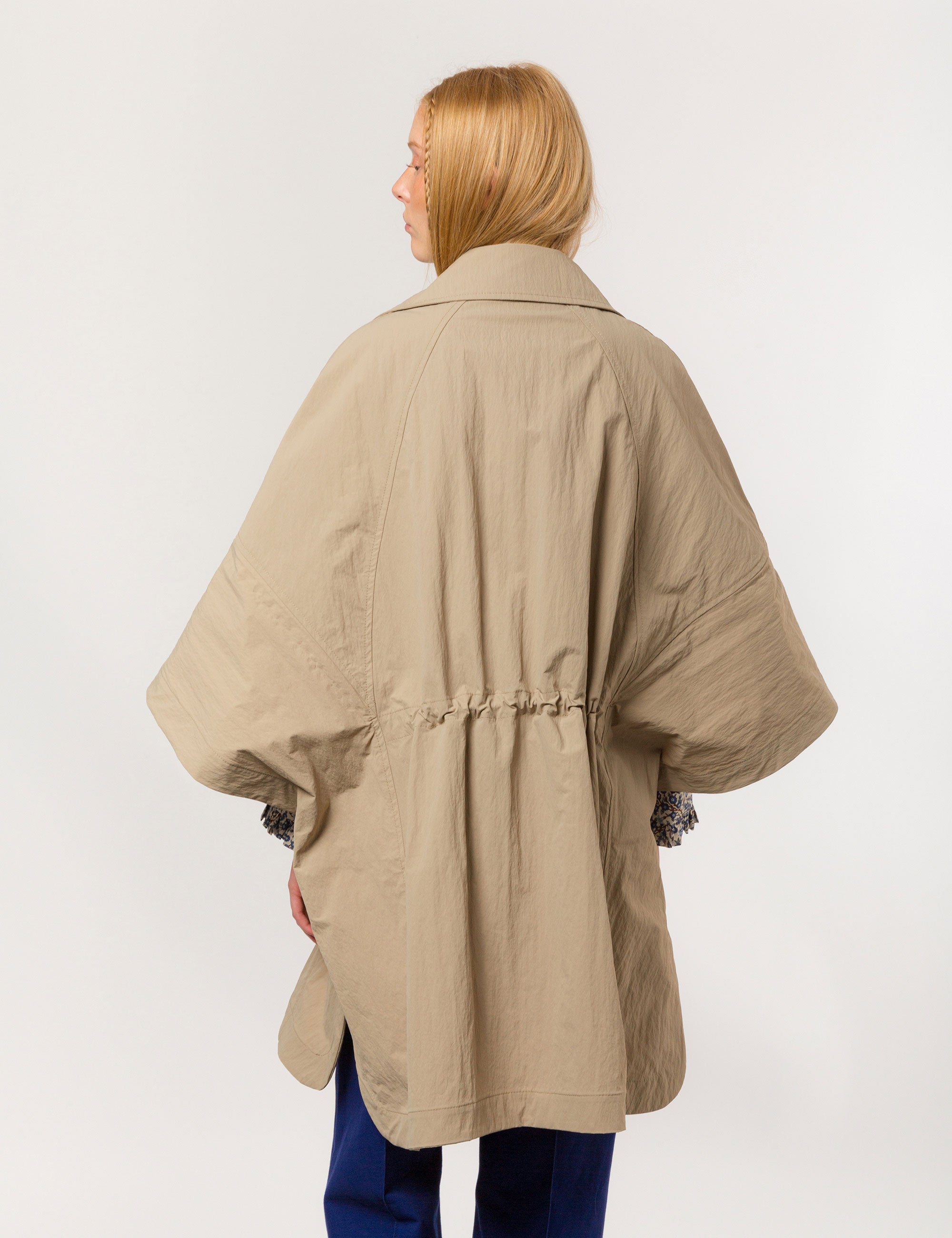 Woman in beige khaki jacket with black buttons, pockets and floral pipings and waist strap