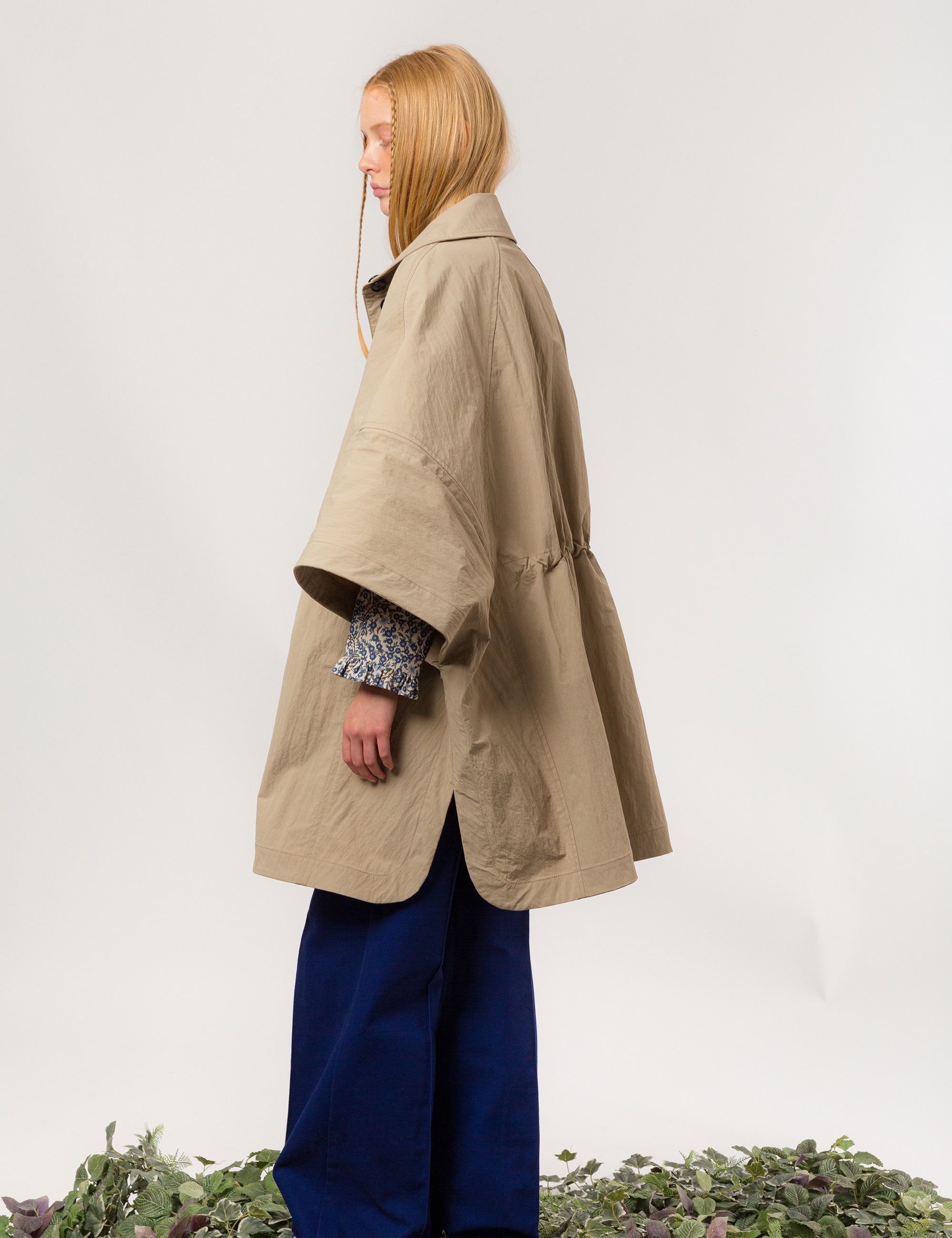 Woman in beige khaki jacket with black buttons, pockets and waist strap and blue trousers