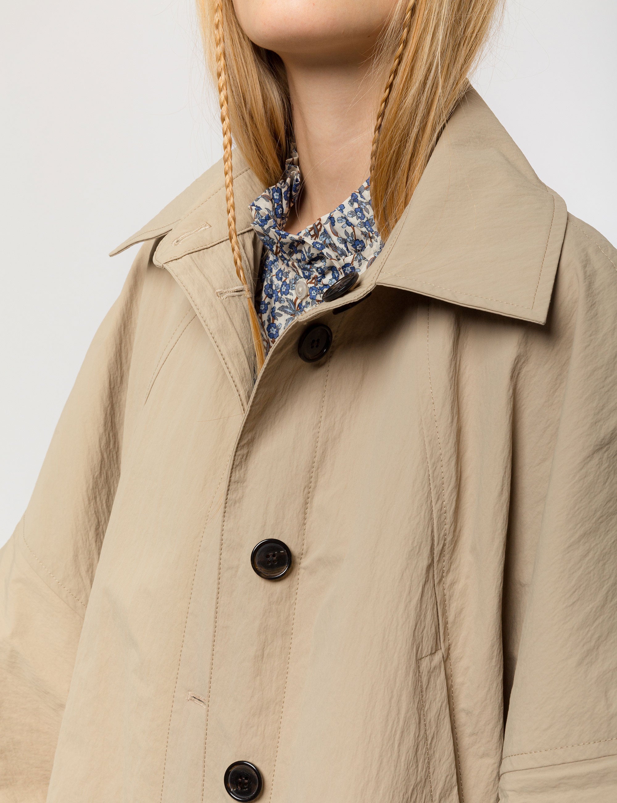 Woman in beige khaki jacket with black buttons and a shirt with blue and white floral pattern