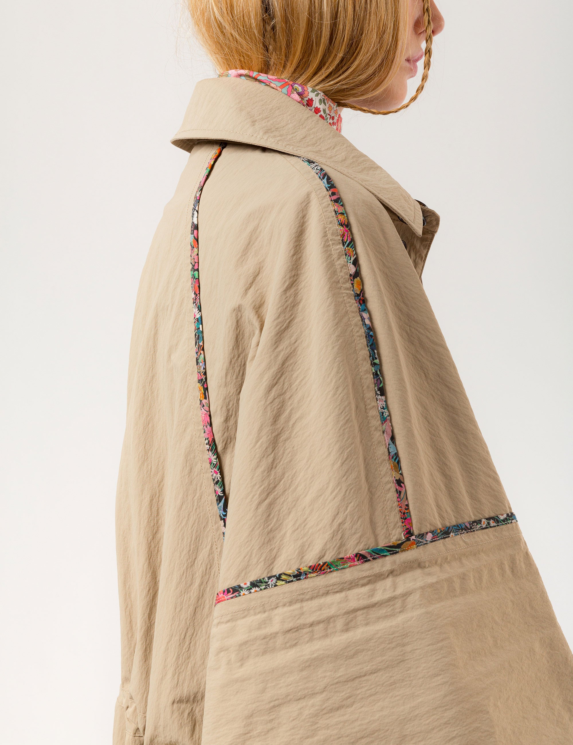 Woman in beige khaki jacket with black buttons, pockets and floral pipings