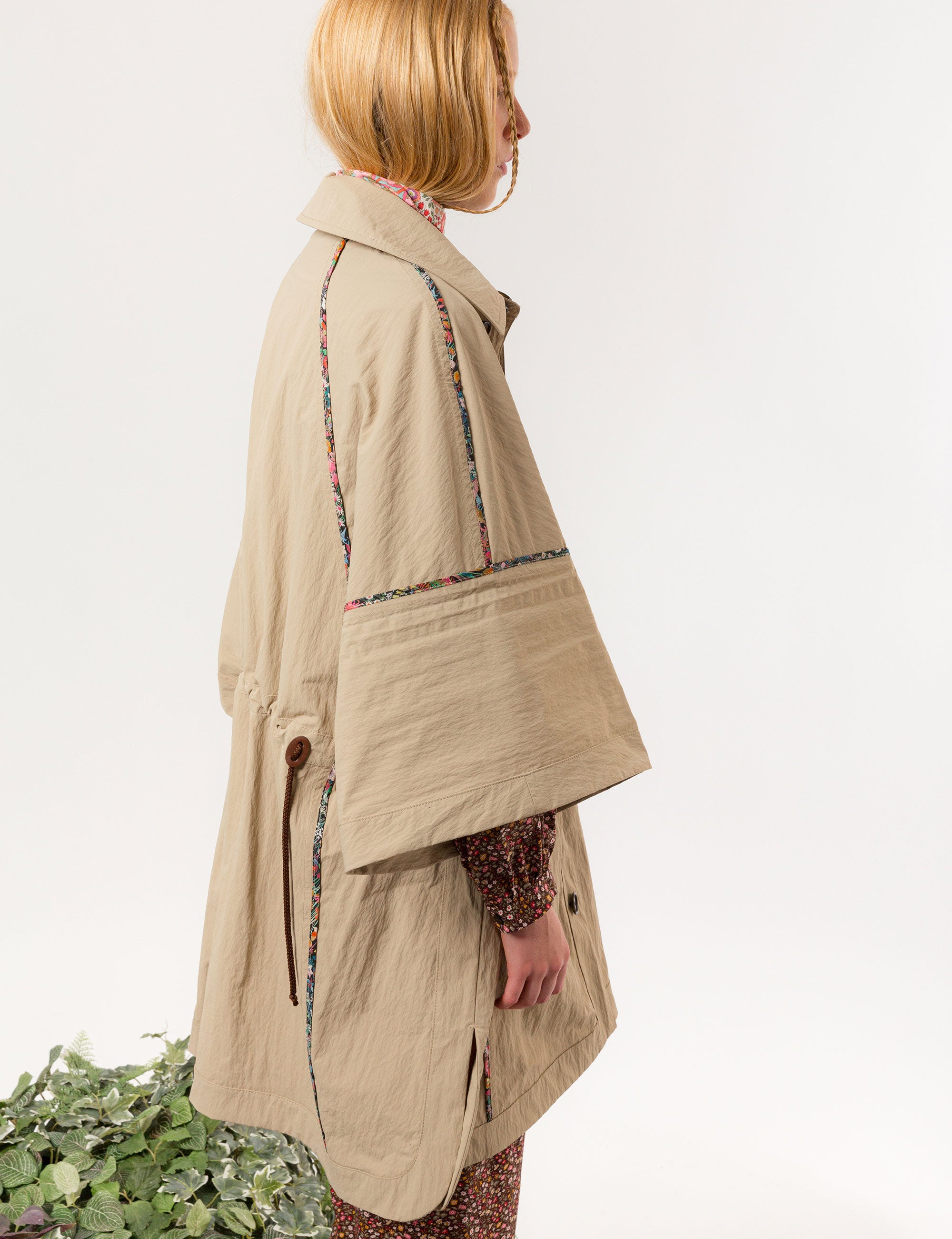 Woman in beige khaki jacket with black buttons, pockets and floral pipings, and brown floral dress