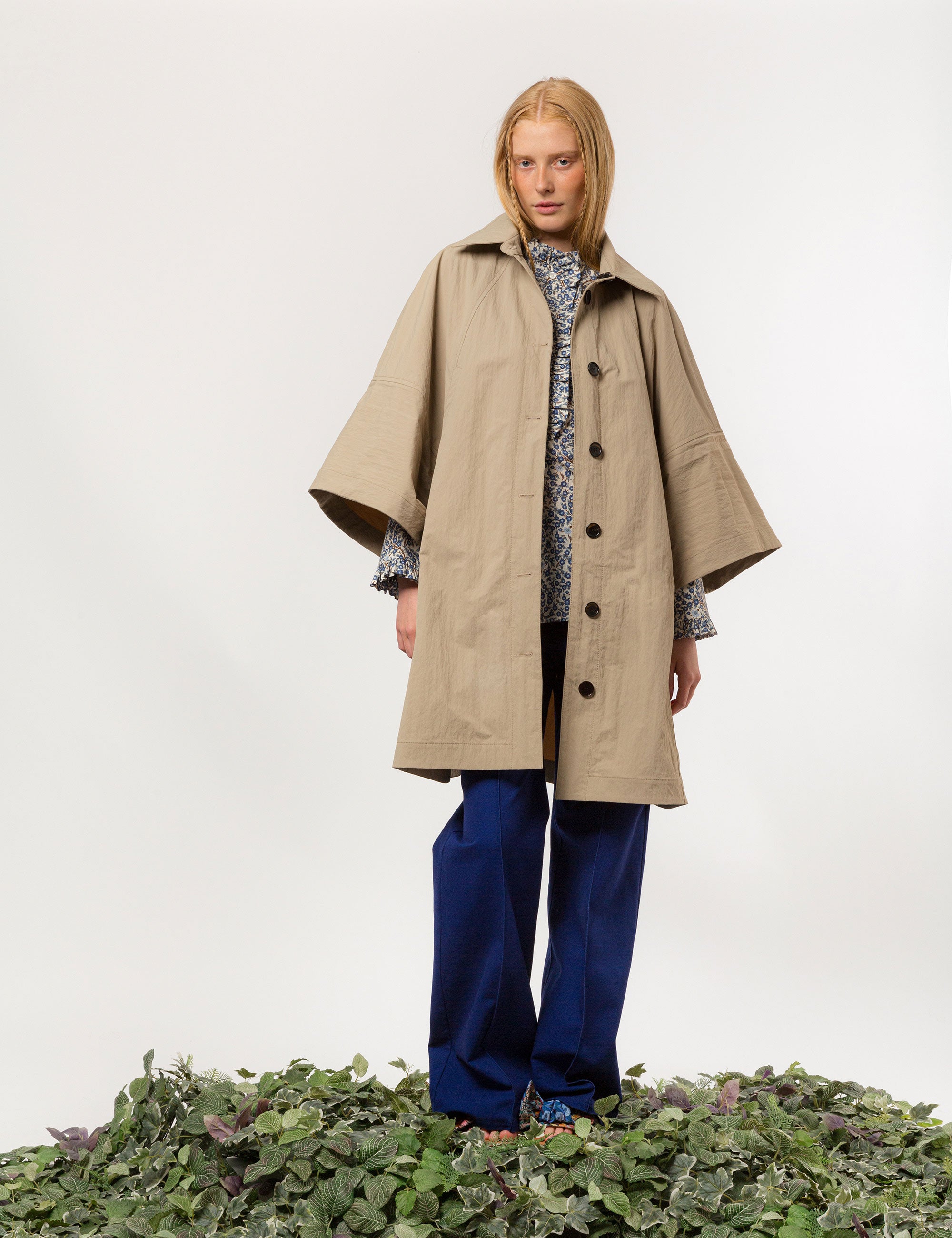 Woman in beige khaki jacket with black buttons and pockets, blue pants and blue and white floral print shirt