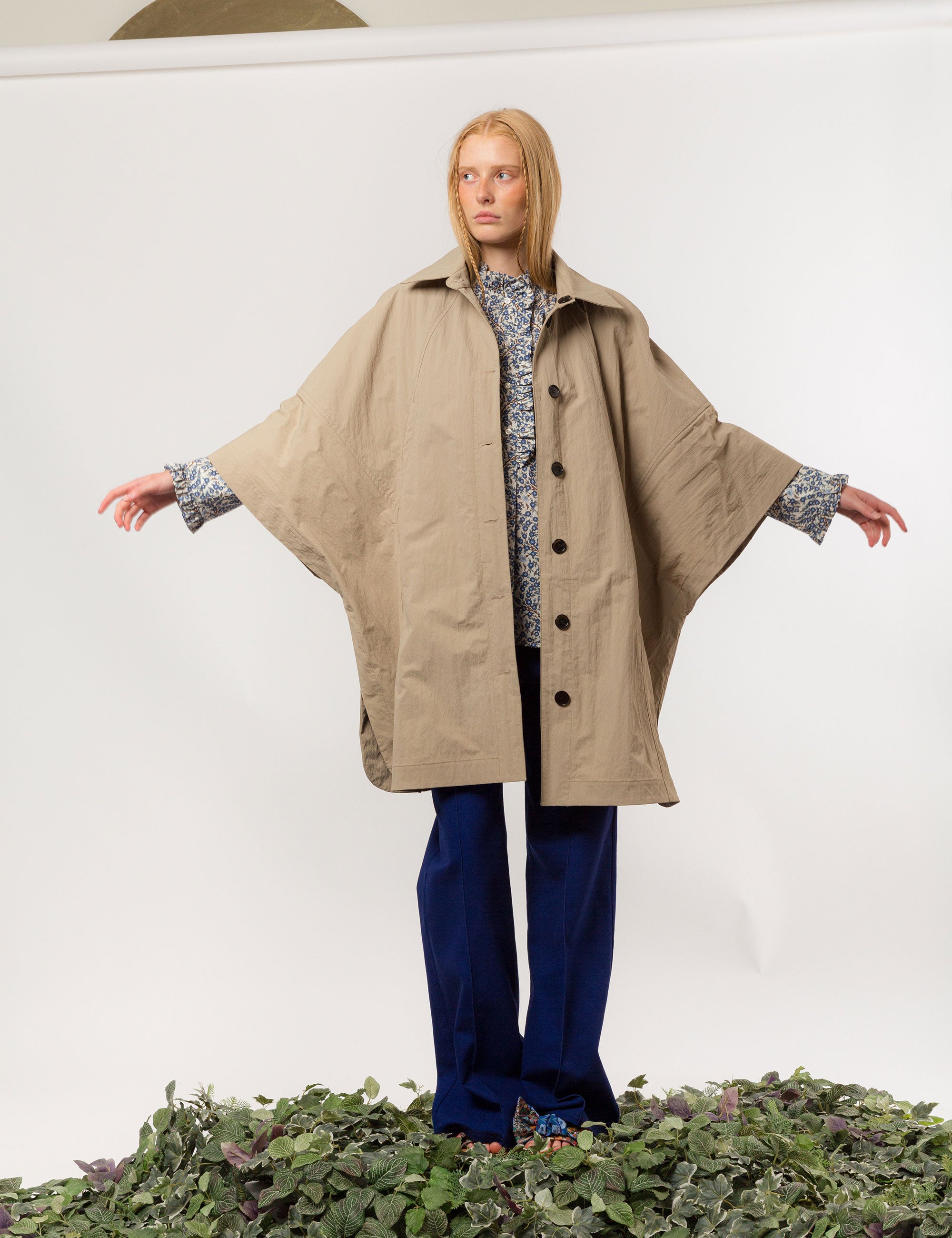 Woman in beige khaki jacket with black buttons and pockets, blue pants and blue and white floral print shirt