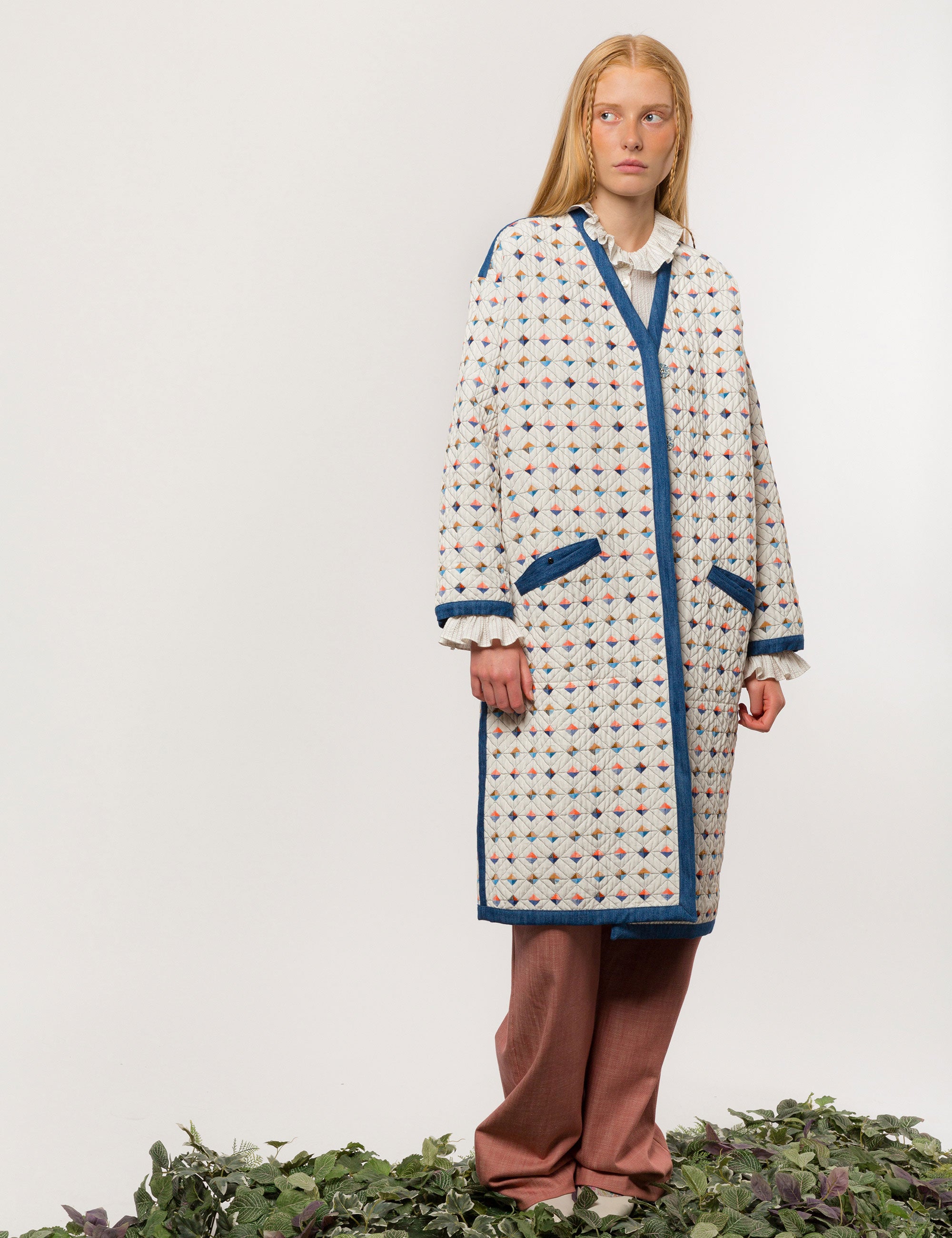 Woman in reversible white quilted coat with multi-colored check print, blue pipings and pockets and dusty pink pants