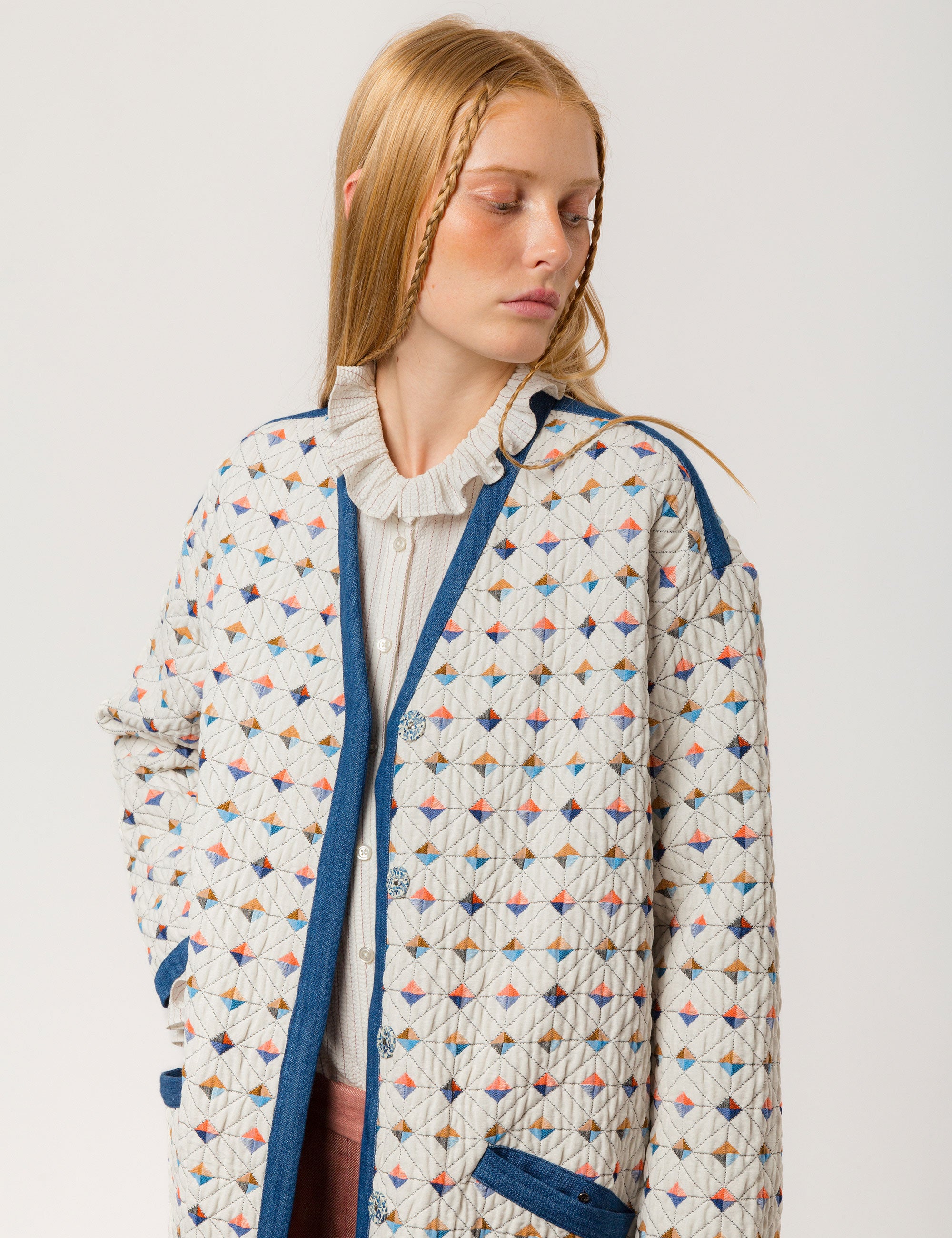 Woman in reversible white quilted coat with multi-colored check print, blue pipings and pockets and white striped shirt with frills