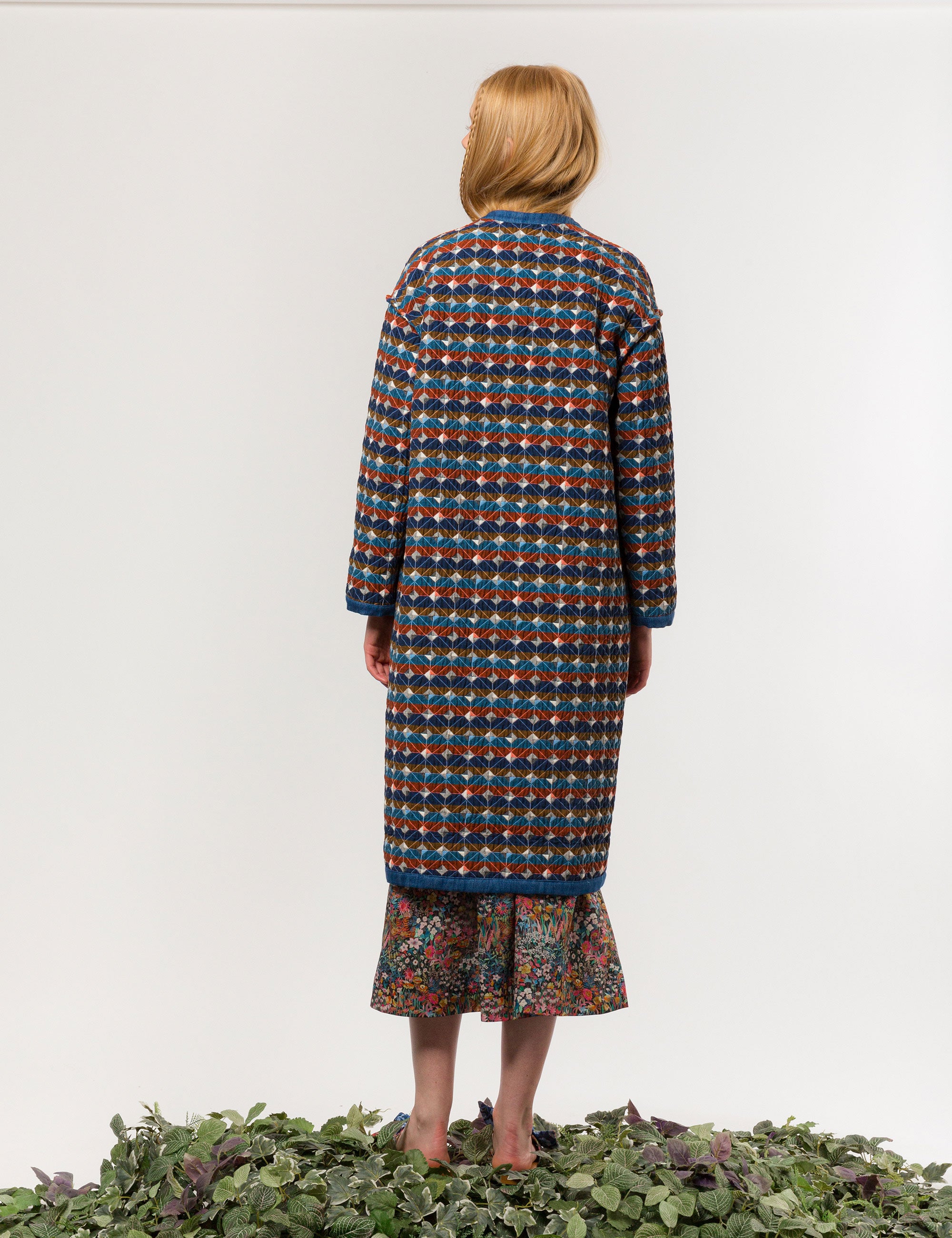 Woman in multi-colored quilted check print coat with blue pipings and large pockets and floral print dress