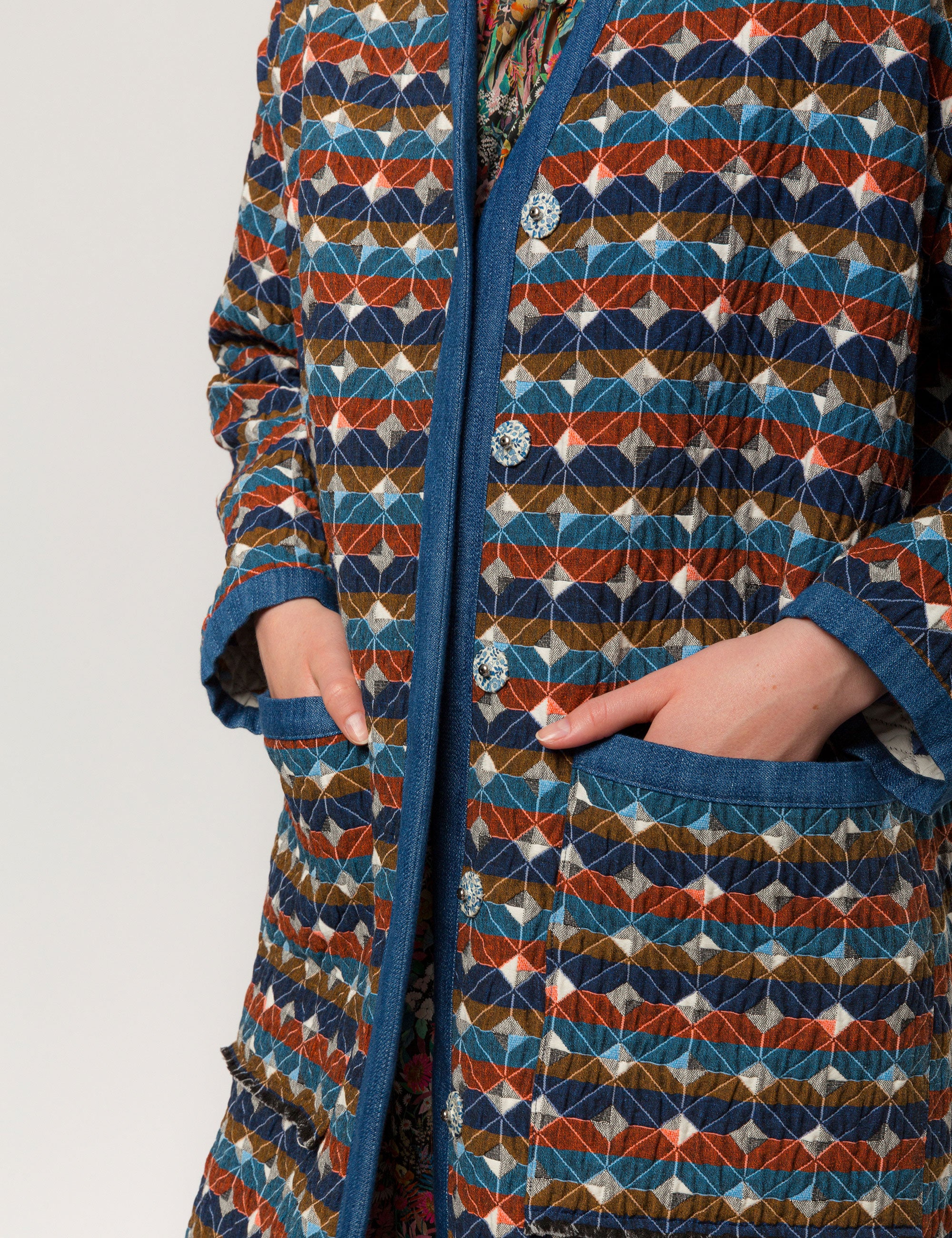 Woman in multi-colored quilted check print coat with blue pipings and large pockets and floral print dress