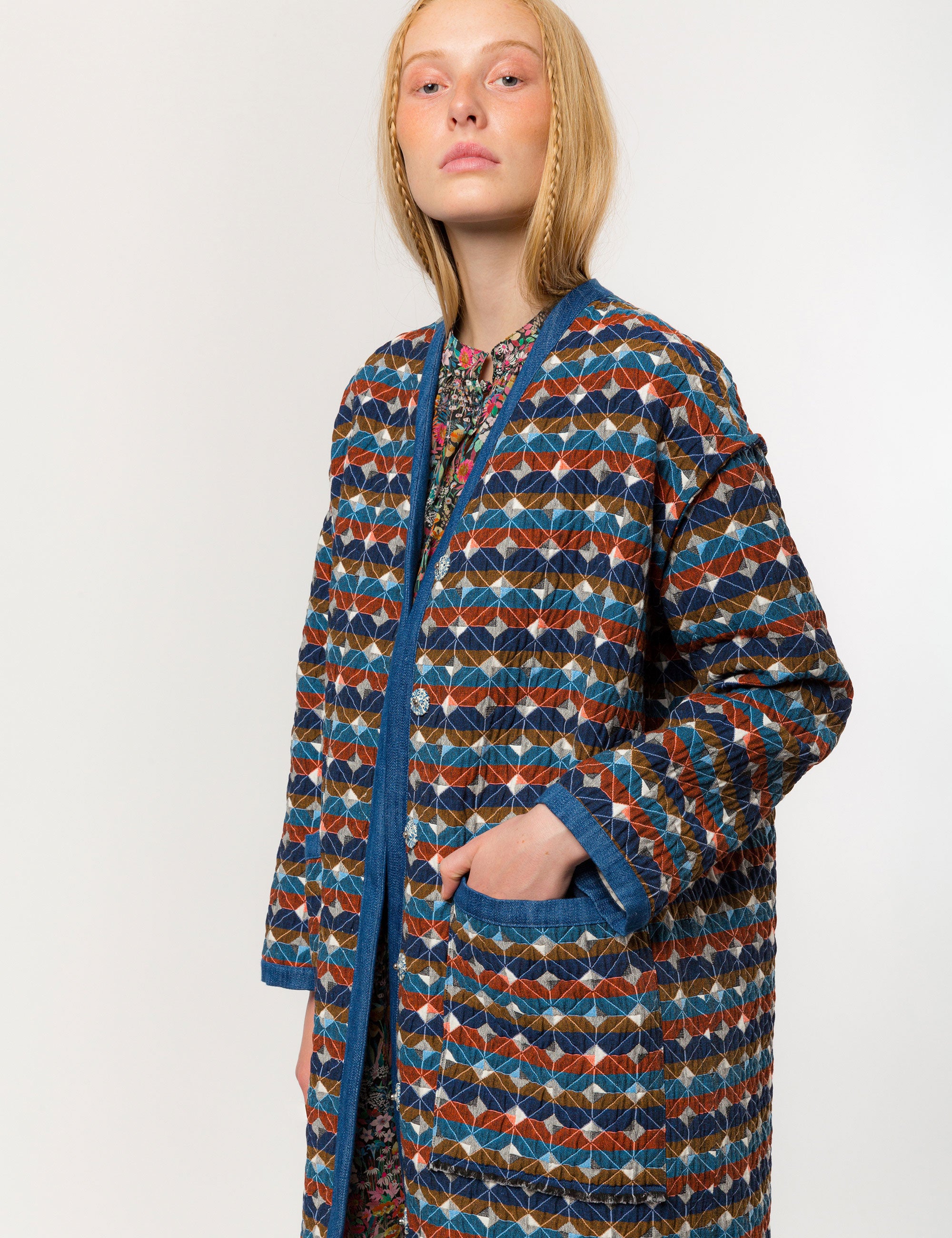 Woman in multi-colored quilted check print coat with blue pipings and large pockets and floral print dress