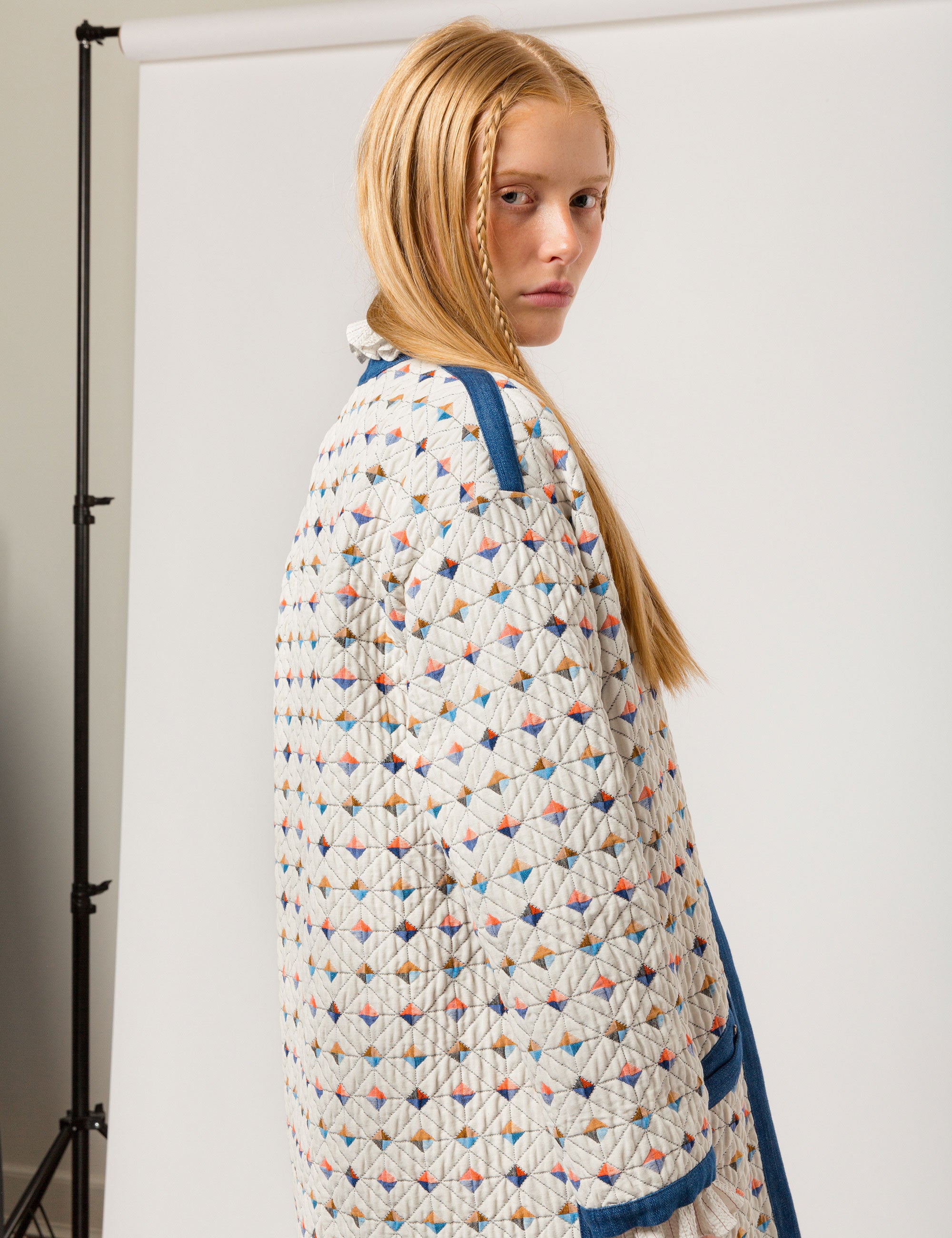 Woman in reversible white quilted coat with multi-colored check print, blue pipings and pockets