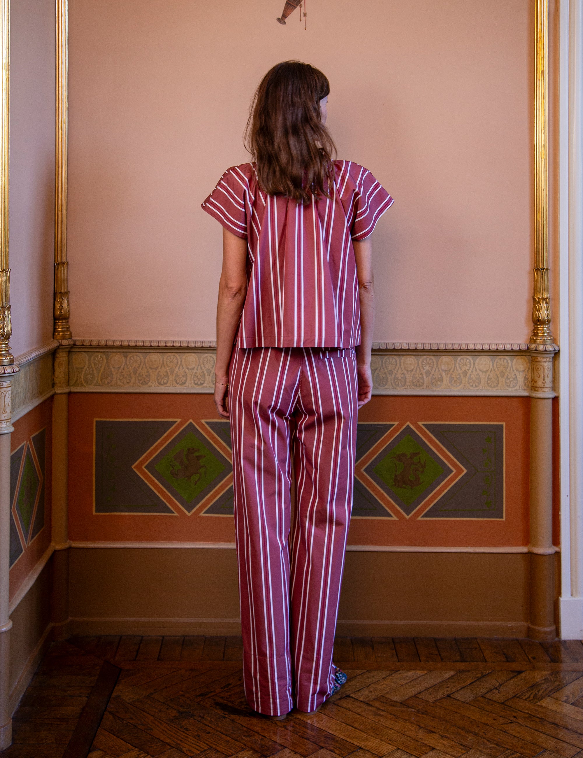 Woman wearing a striped outfit standing in a room with decorative walls.