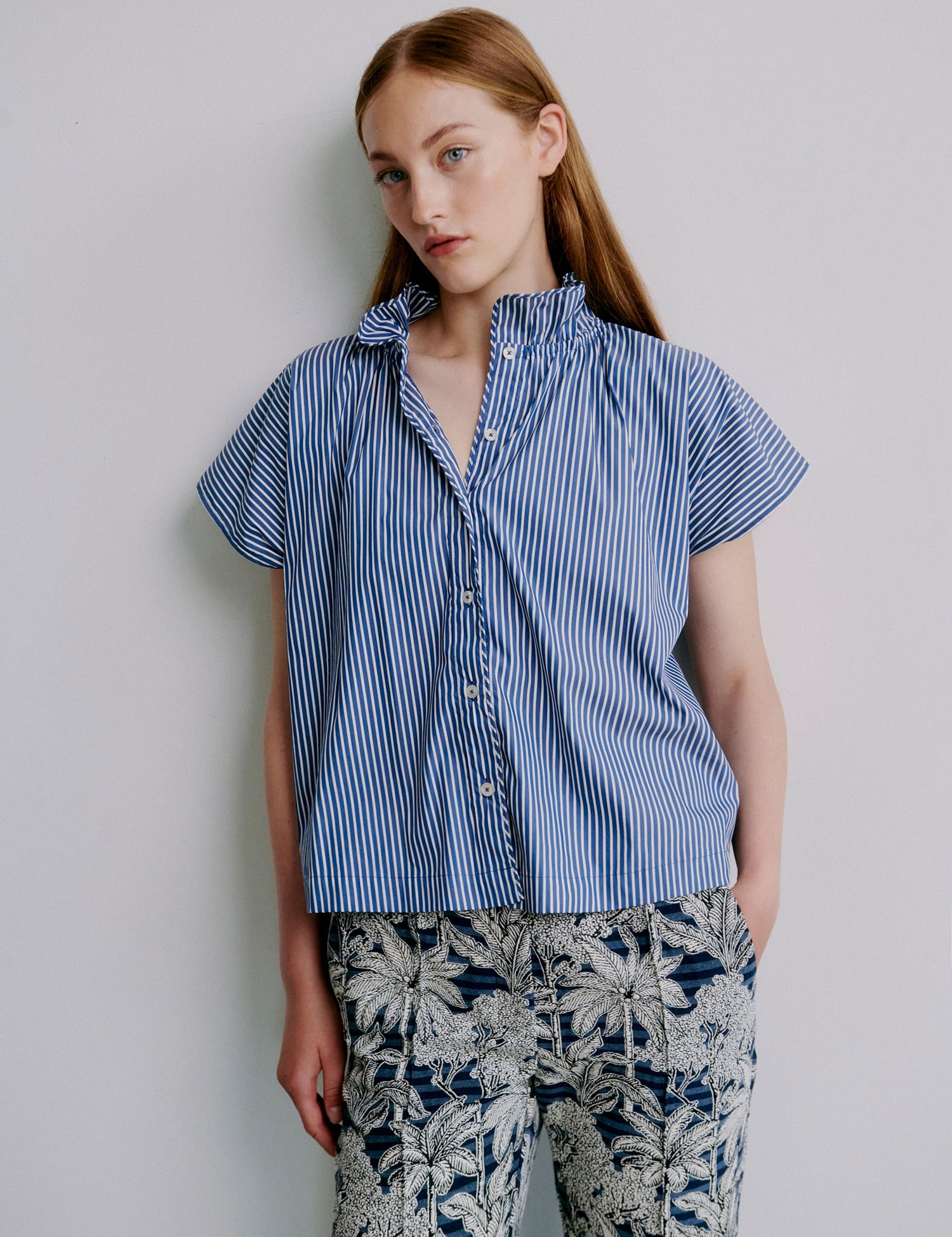 Woman wearing a blue striped shirt and floral pants against a plain background