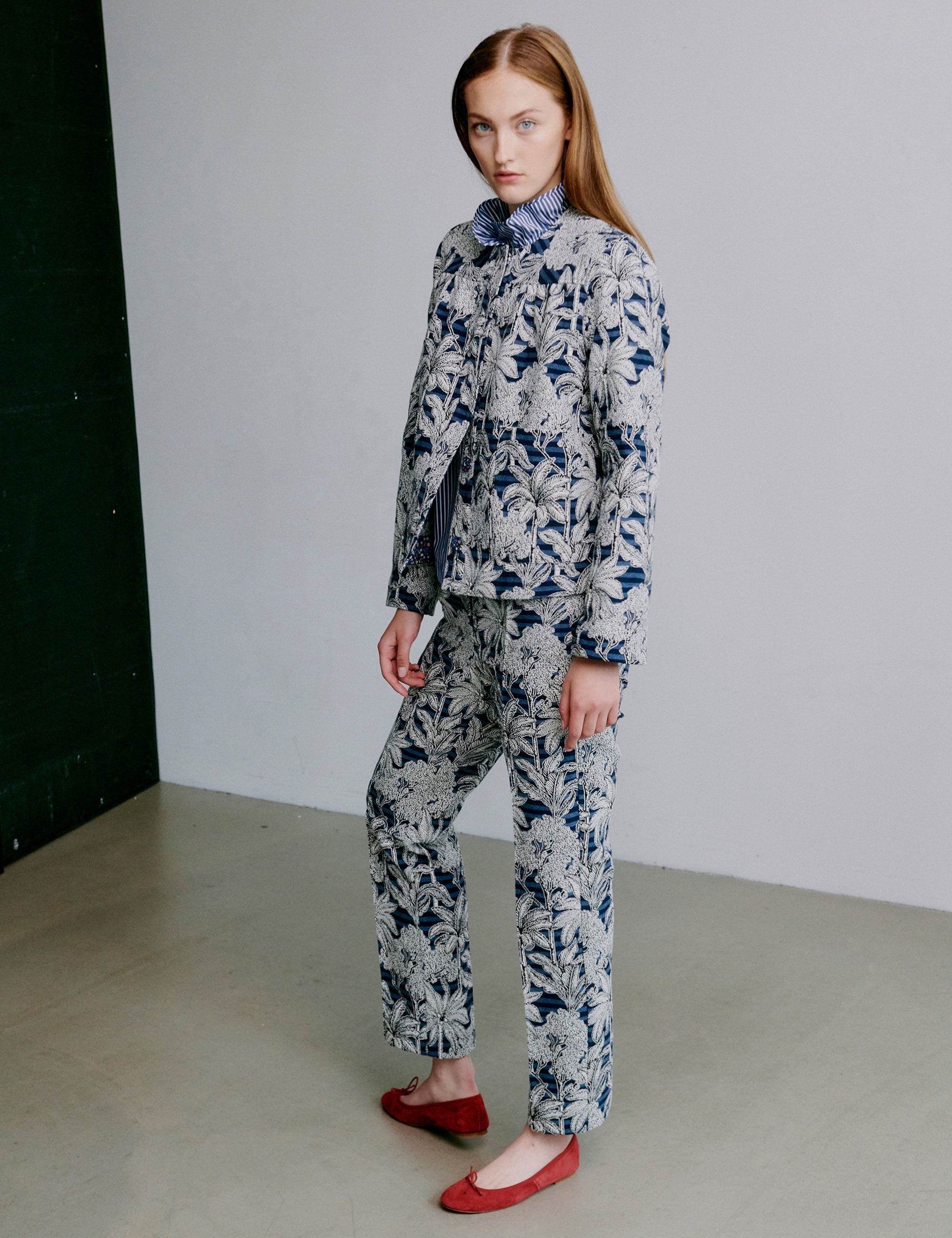 Woman wearing a blue floral patterned jacket with matching pants on a plain background