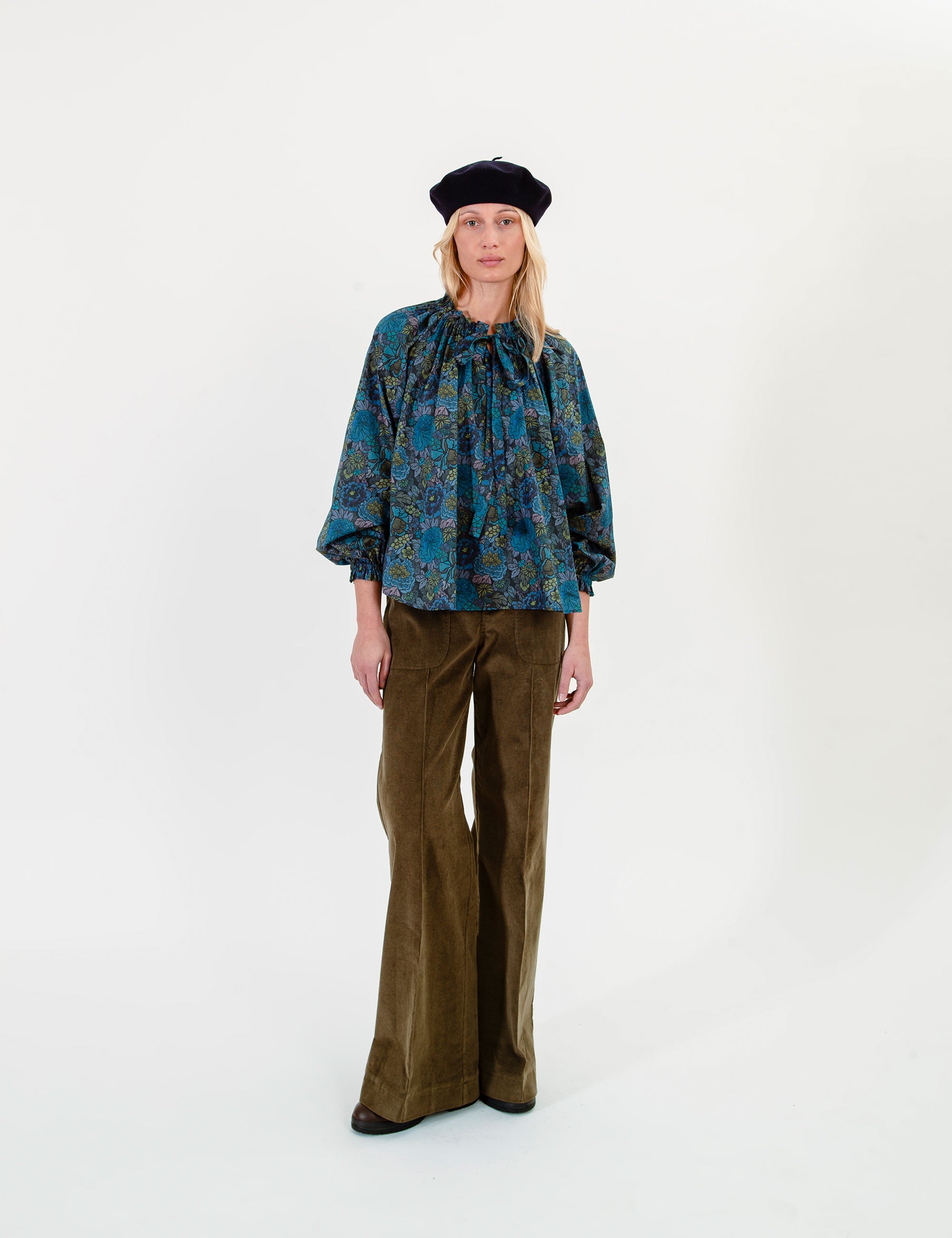 Woman wearing a floral patterned blue blouse and olive green pants on a white background