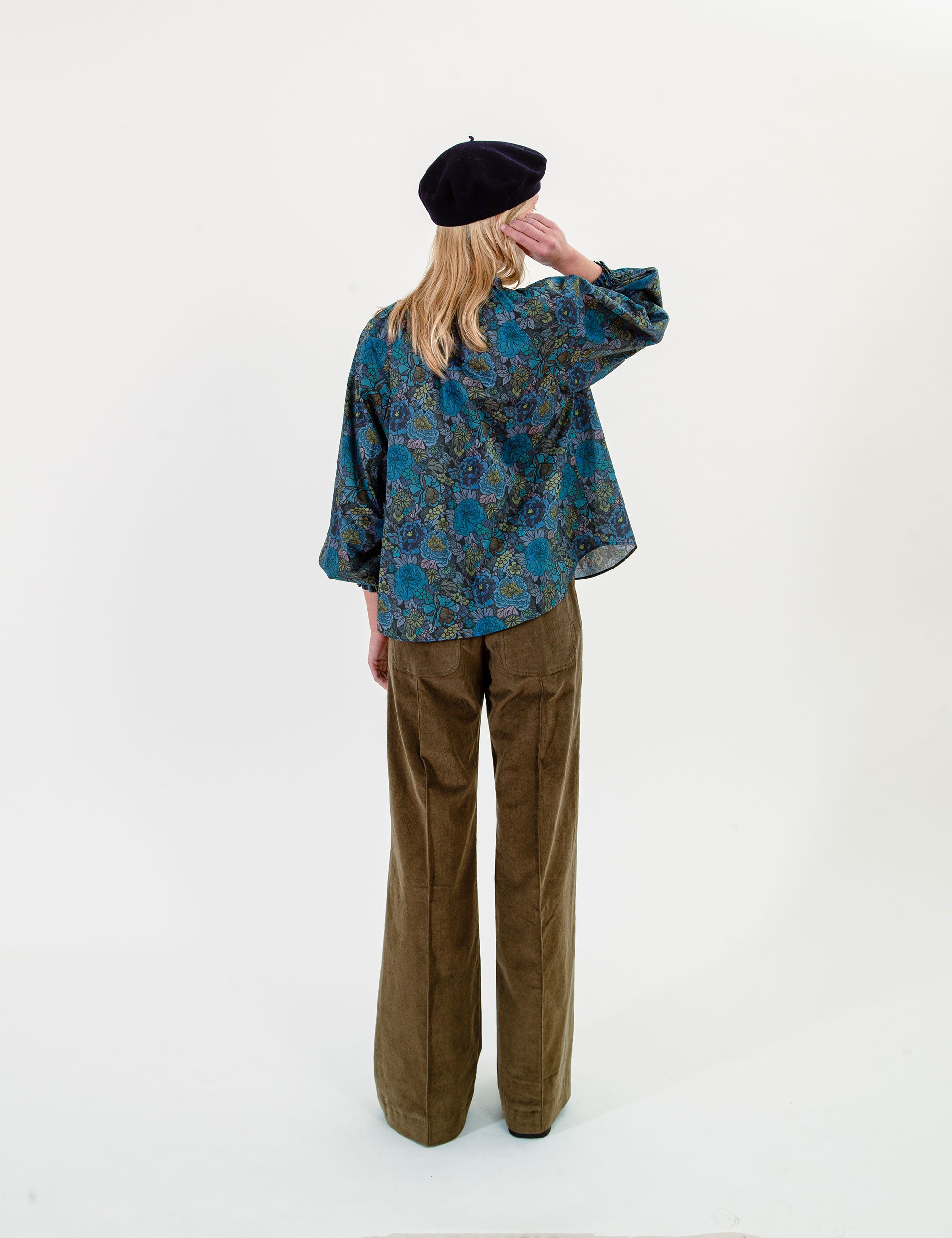 Woman wearing a floral patterned blue blouse and olive green pants on a white background