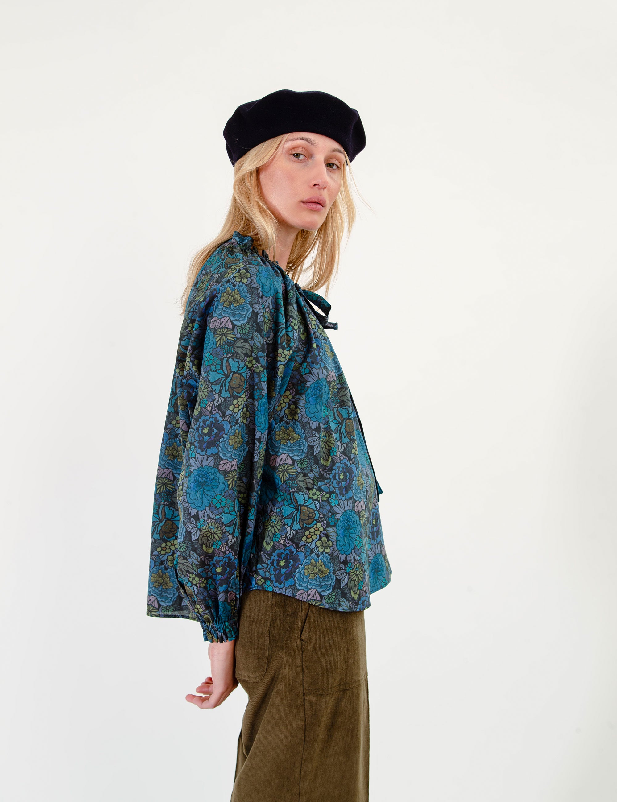 Woman wearing a floral patterned blue blouse and olive green pants on a white background