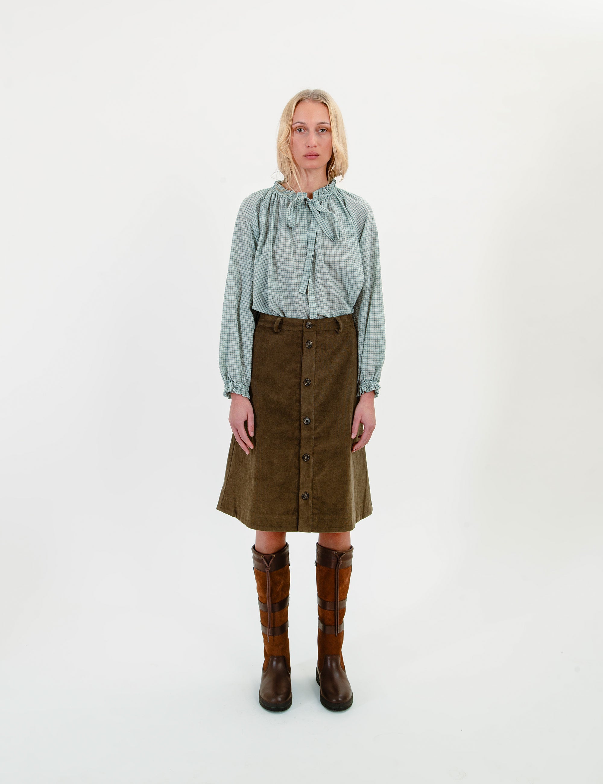 Woman wearing a light gree shirt, green skirt, and brown boots on a white background