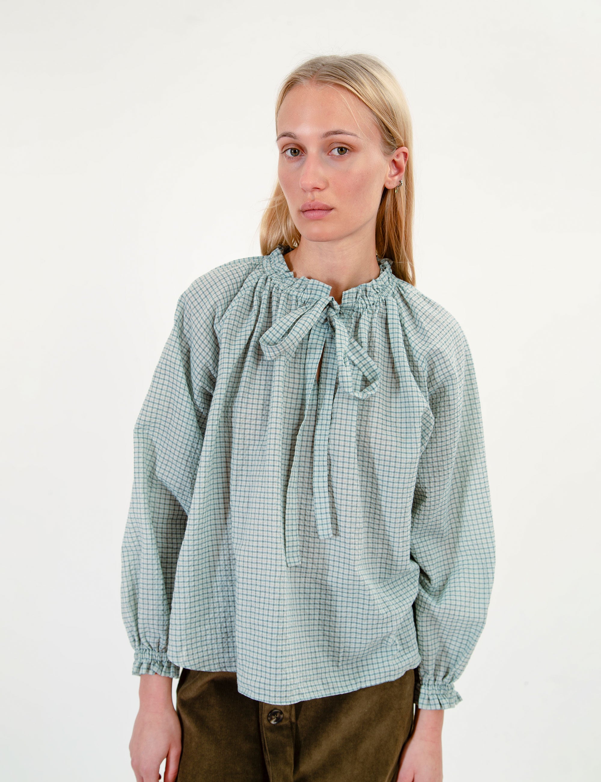 Woman wearing a green checkered blouse with ruffles and a bow on a white background