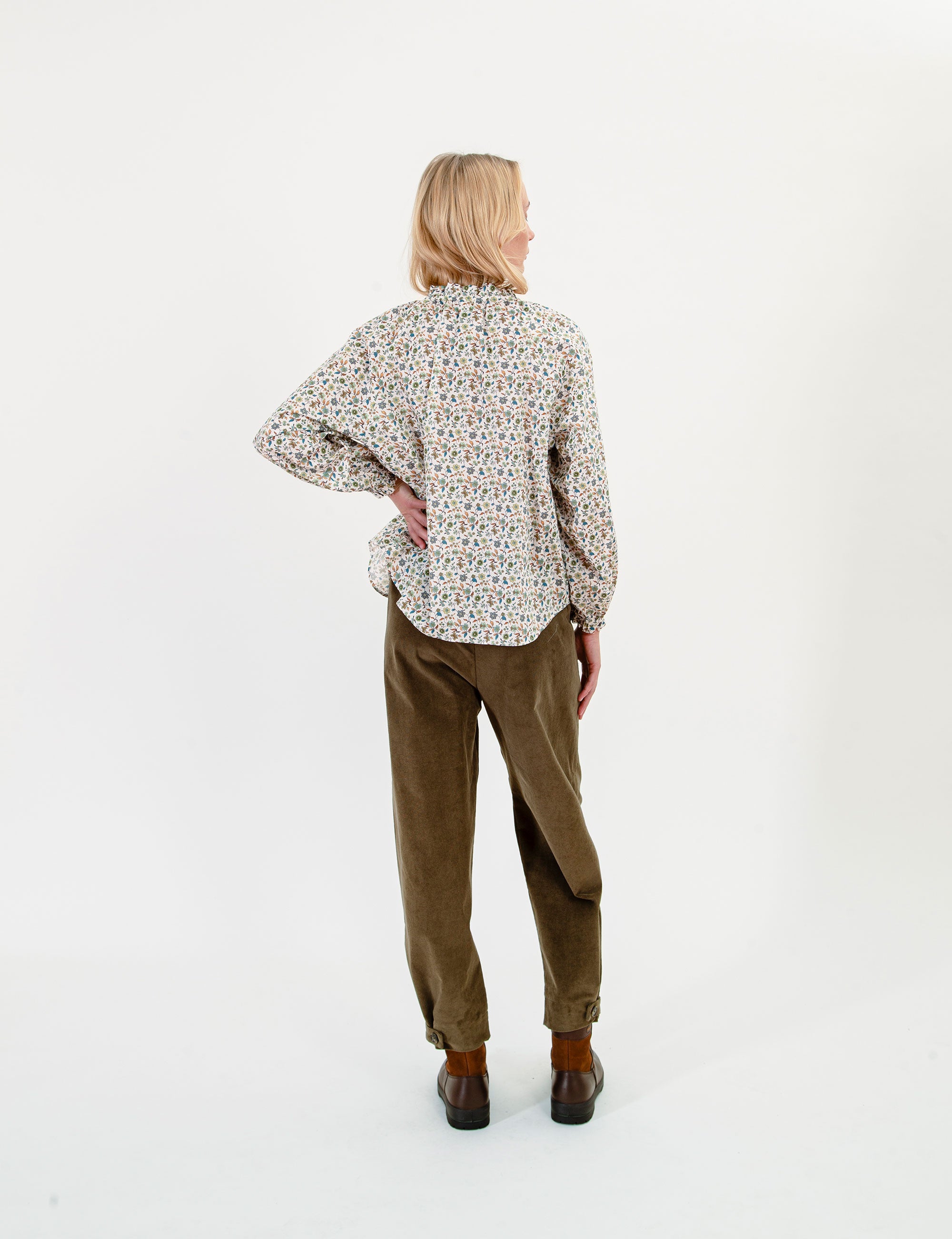 Woman wearing a patterned blouse and olive green corduroy pants on a white background