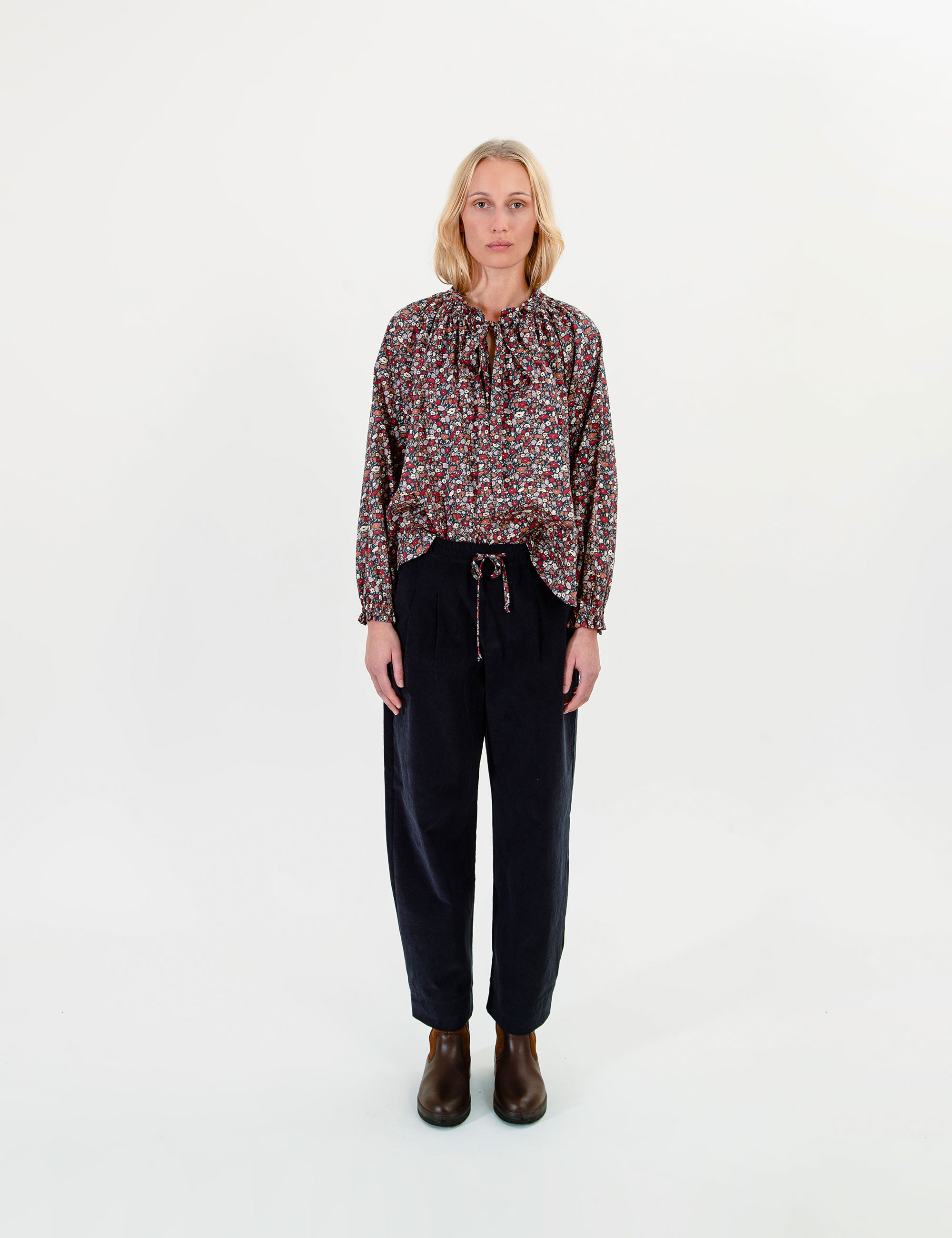Woman wearing a patterned blouse and dark pants on a white background