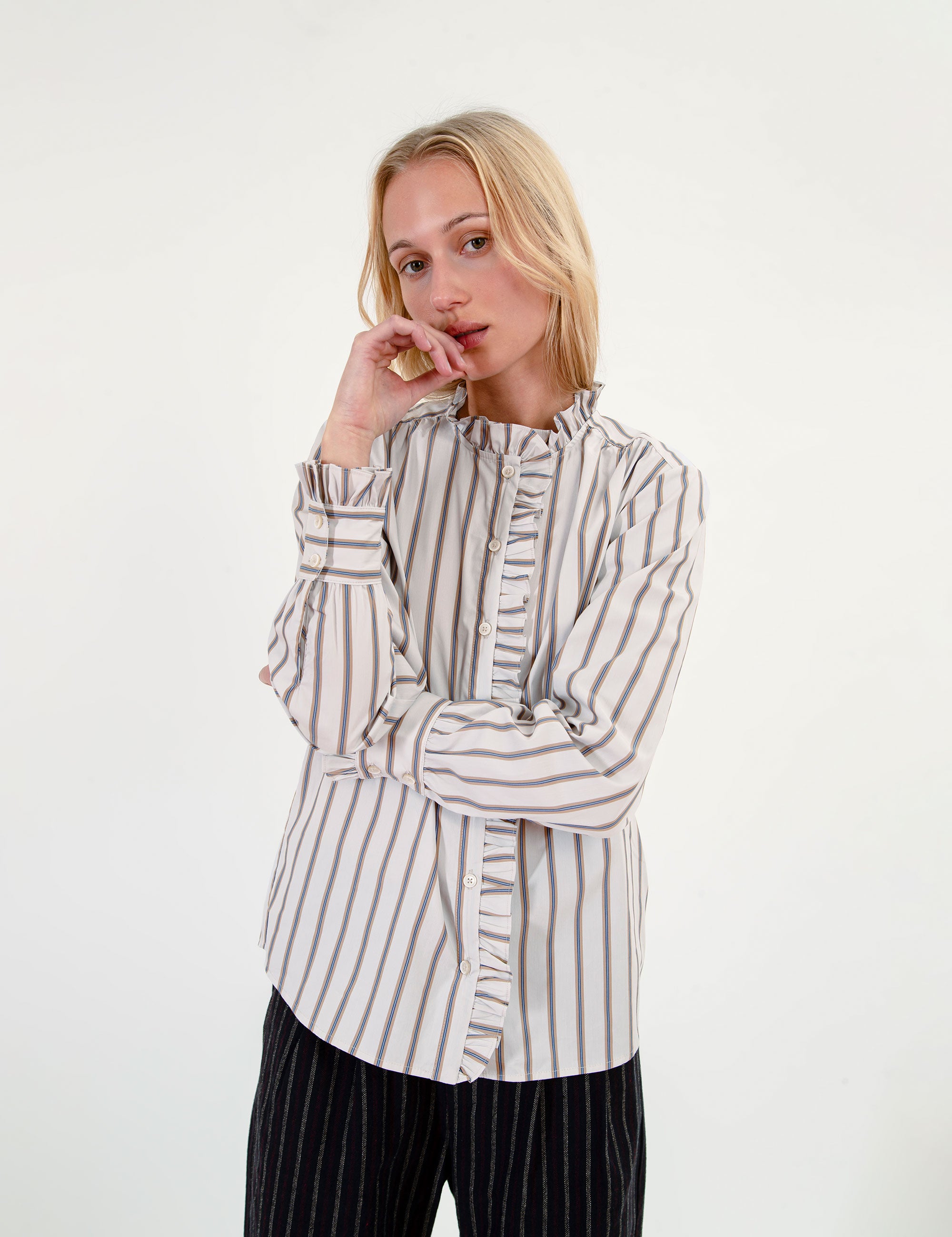 Woman wearing a striped ruffled shirt and black pants on a white background