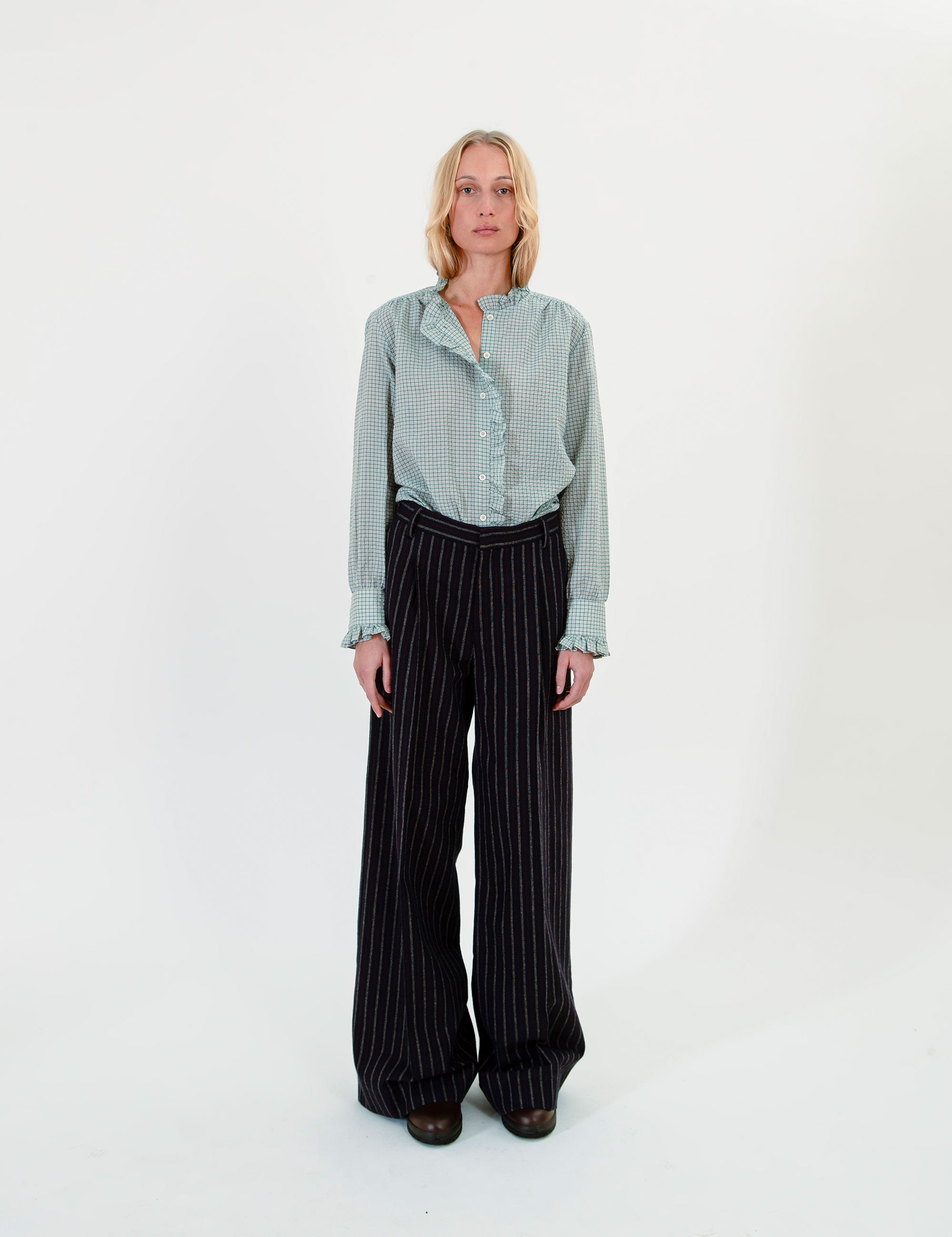 Woman wearing a light green checkered shirt and black pinstripe pants on a white background