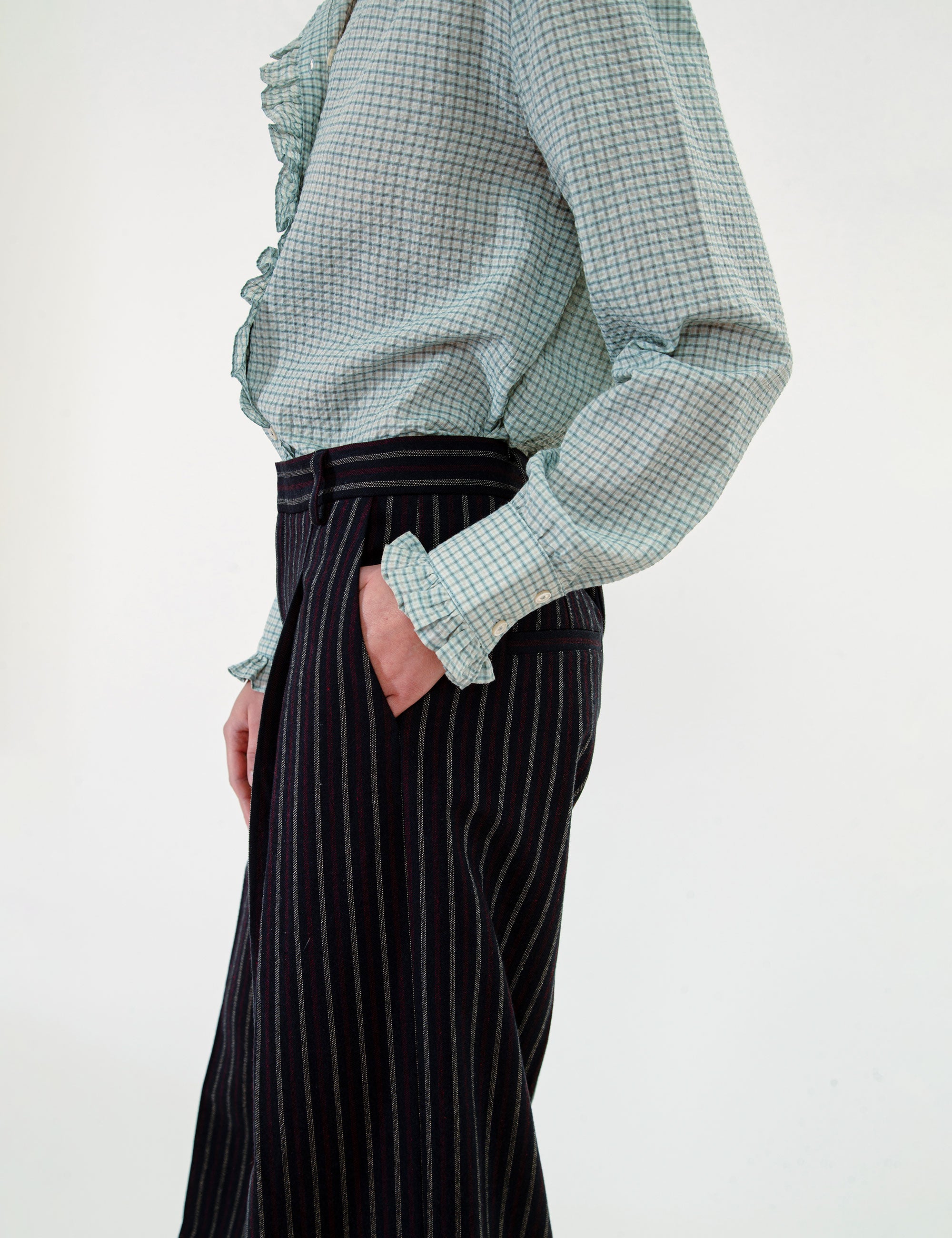 Woman wearing a green checkered blouse and black pinstripe pants on a white background