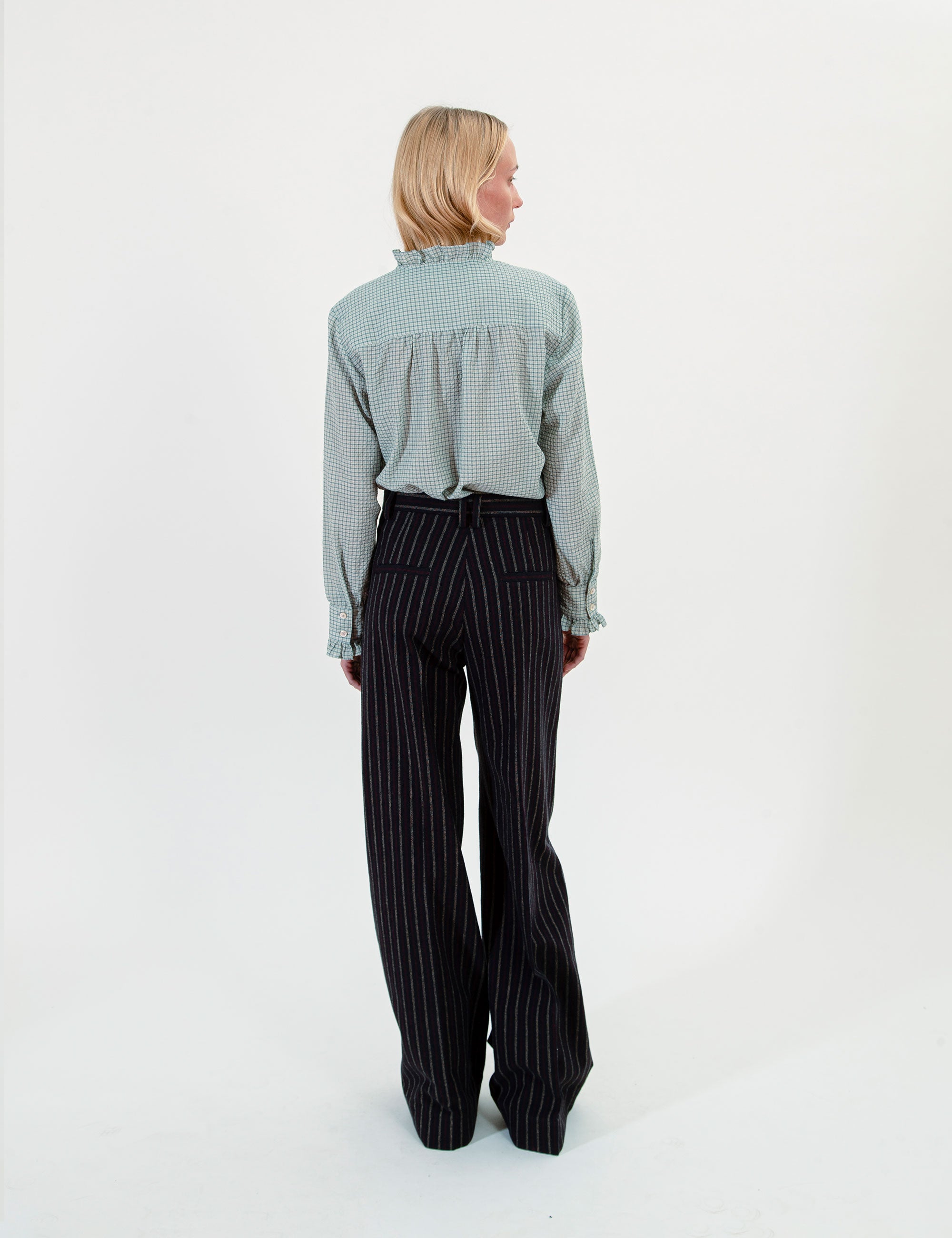 Woman wearing a light green checkered shirt and black pinstripe pants on a white background