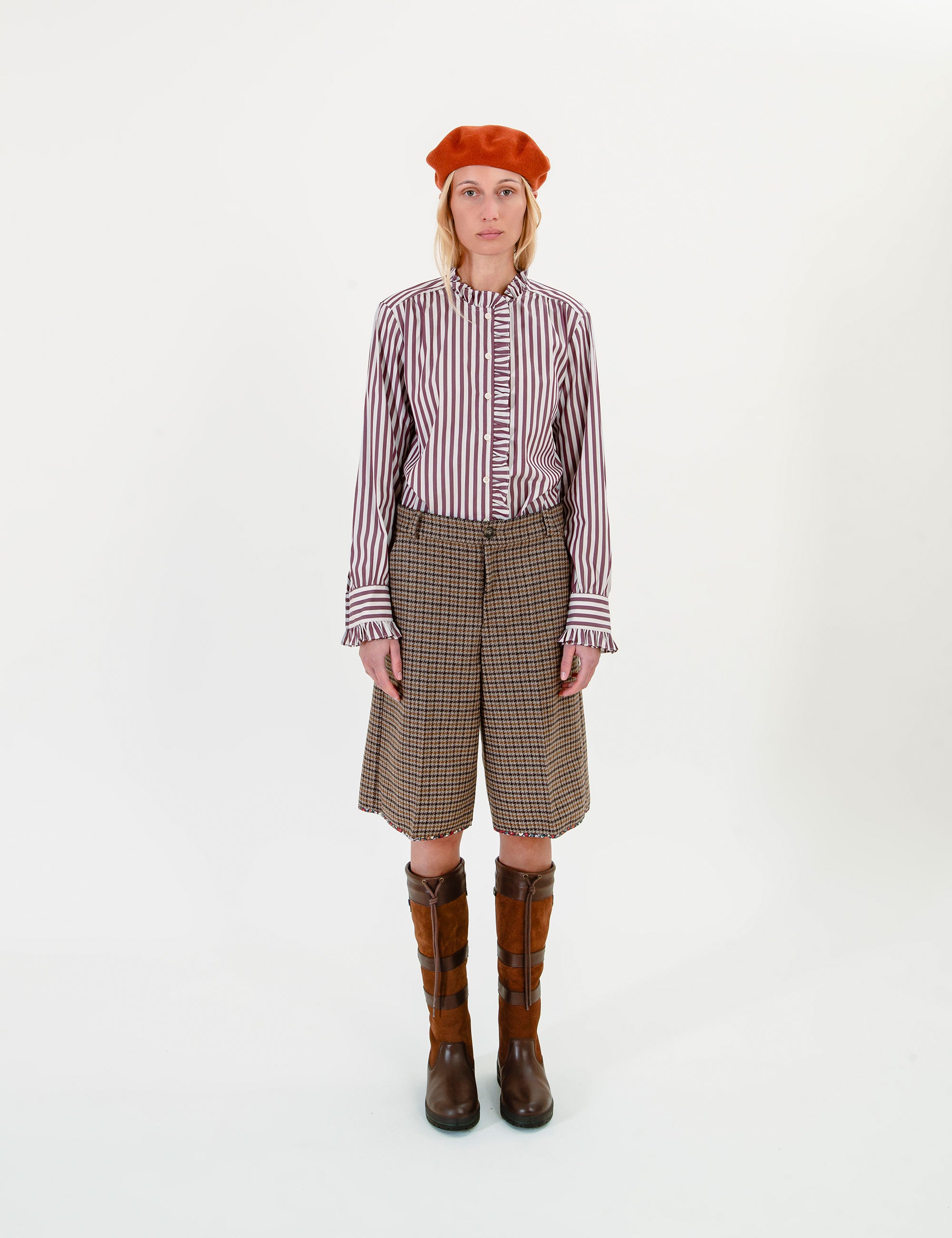 Woman wearing a striped ruffle shirt, plaid shorts, and brown boots on a white background