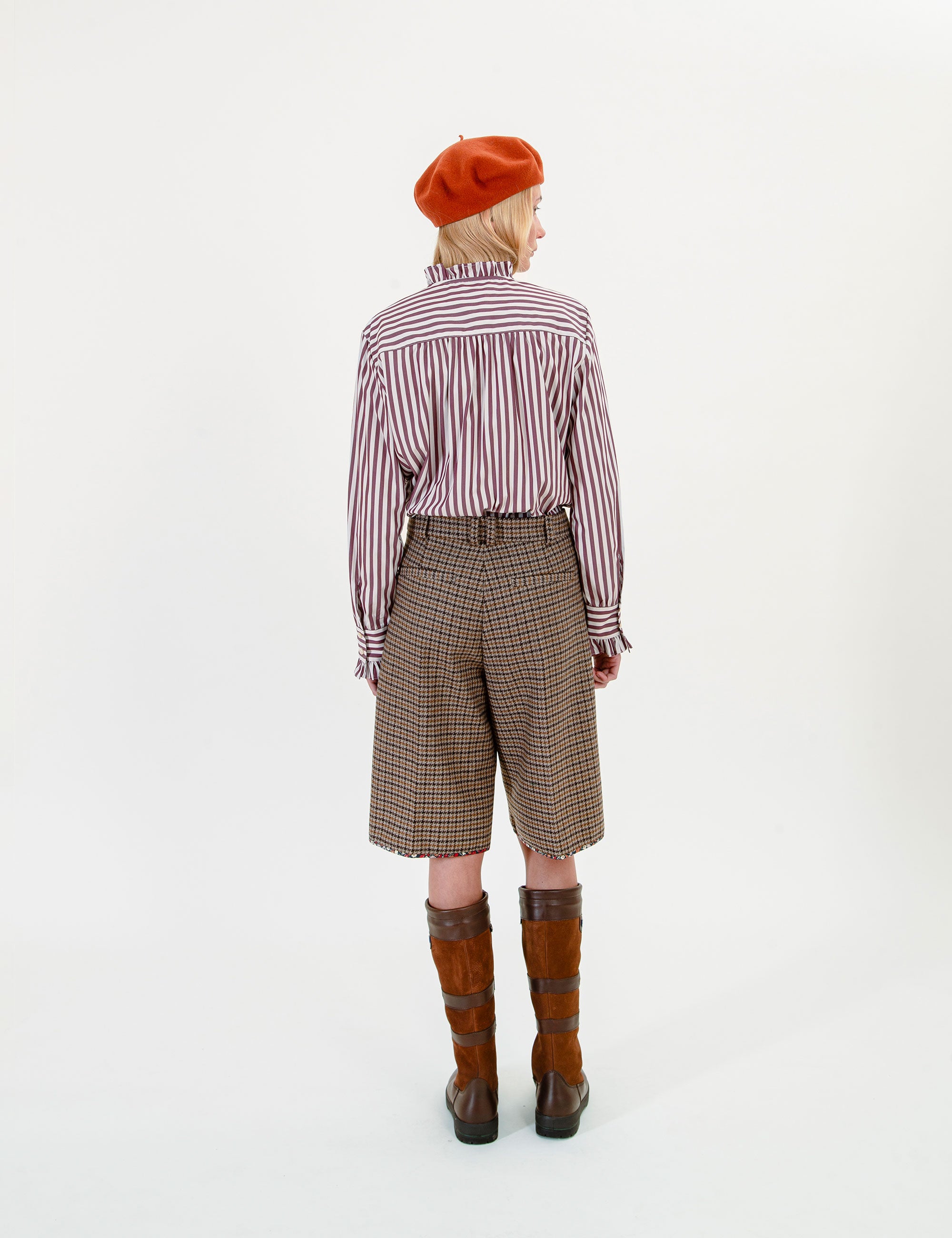 Woman wearing a striped ruffle shirt, plaid shorts, and brown boots on a white background