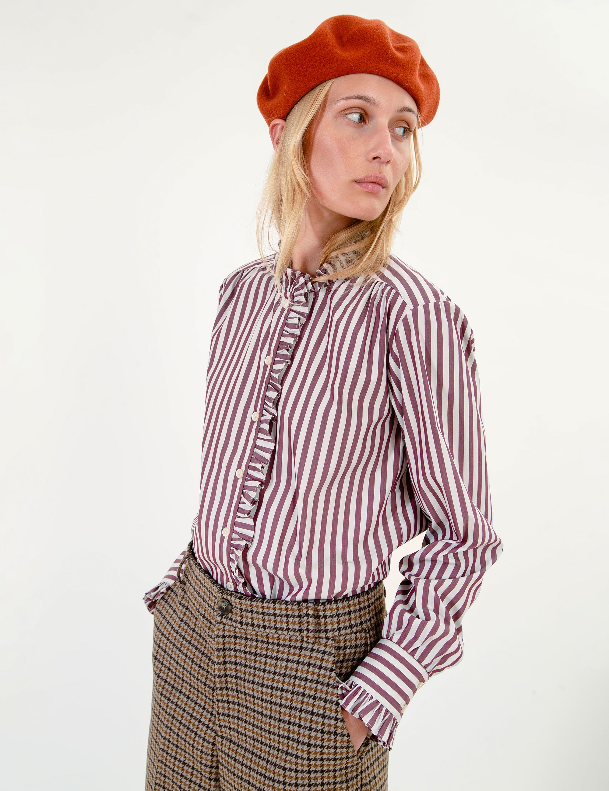 Woman wearing a striped ruffle shirt, plaid shorts, and brown boots on a white background