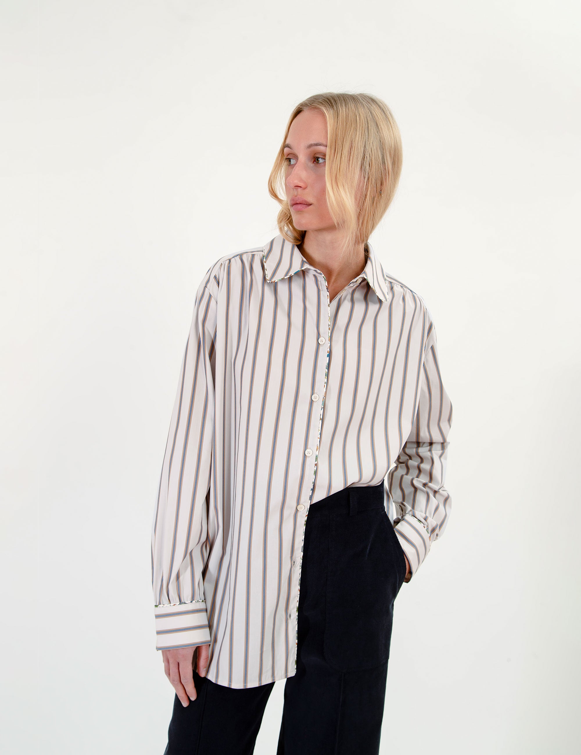 Woman wearing an oversized striped shirt and black pants holding a patterned scarf on a white background