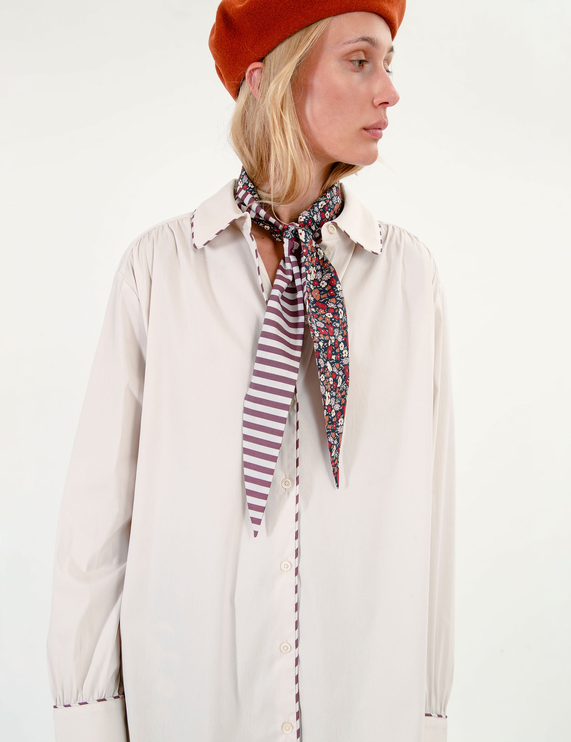 Woman wearing a beige shirt, orange beret, striped and floral scarf