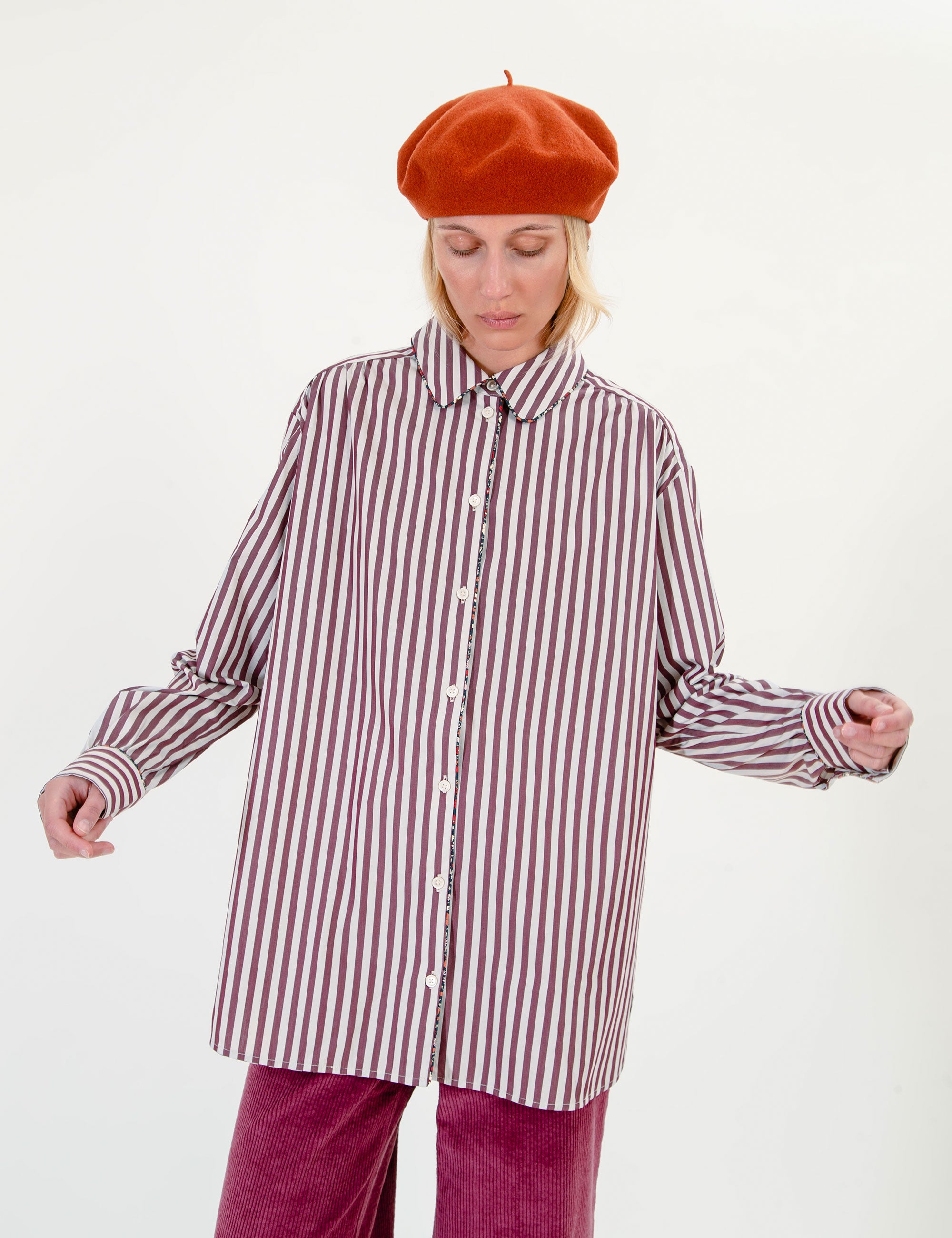 Woman wearing a striped shirt, orange  beret, and pink pants on a white background