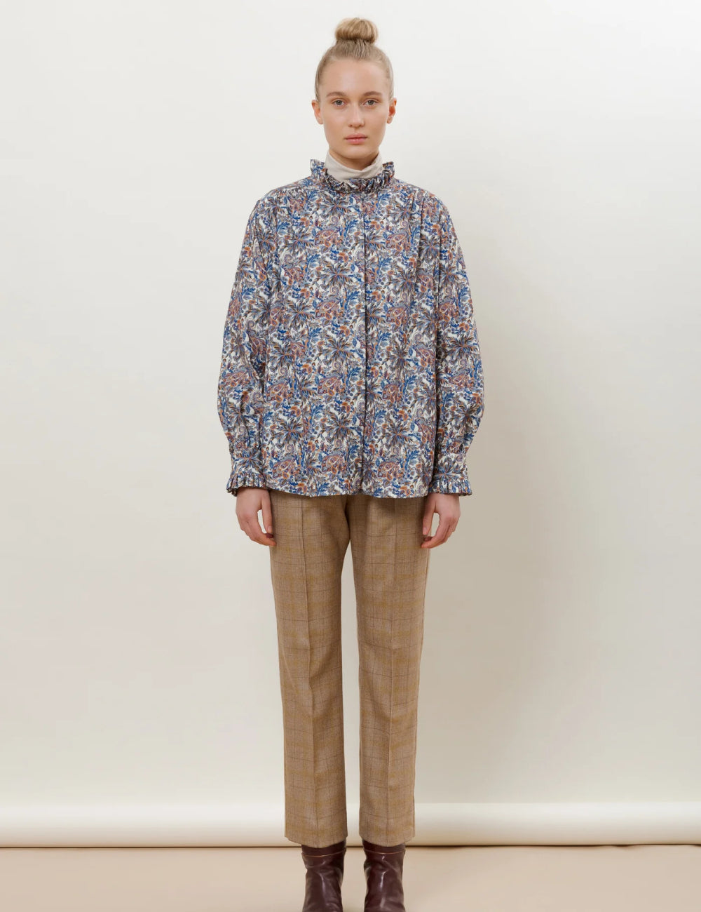 Woman in shirt jacket in red blue and grey paisley pattern with frilled stand collar and beige checked wool pants