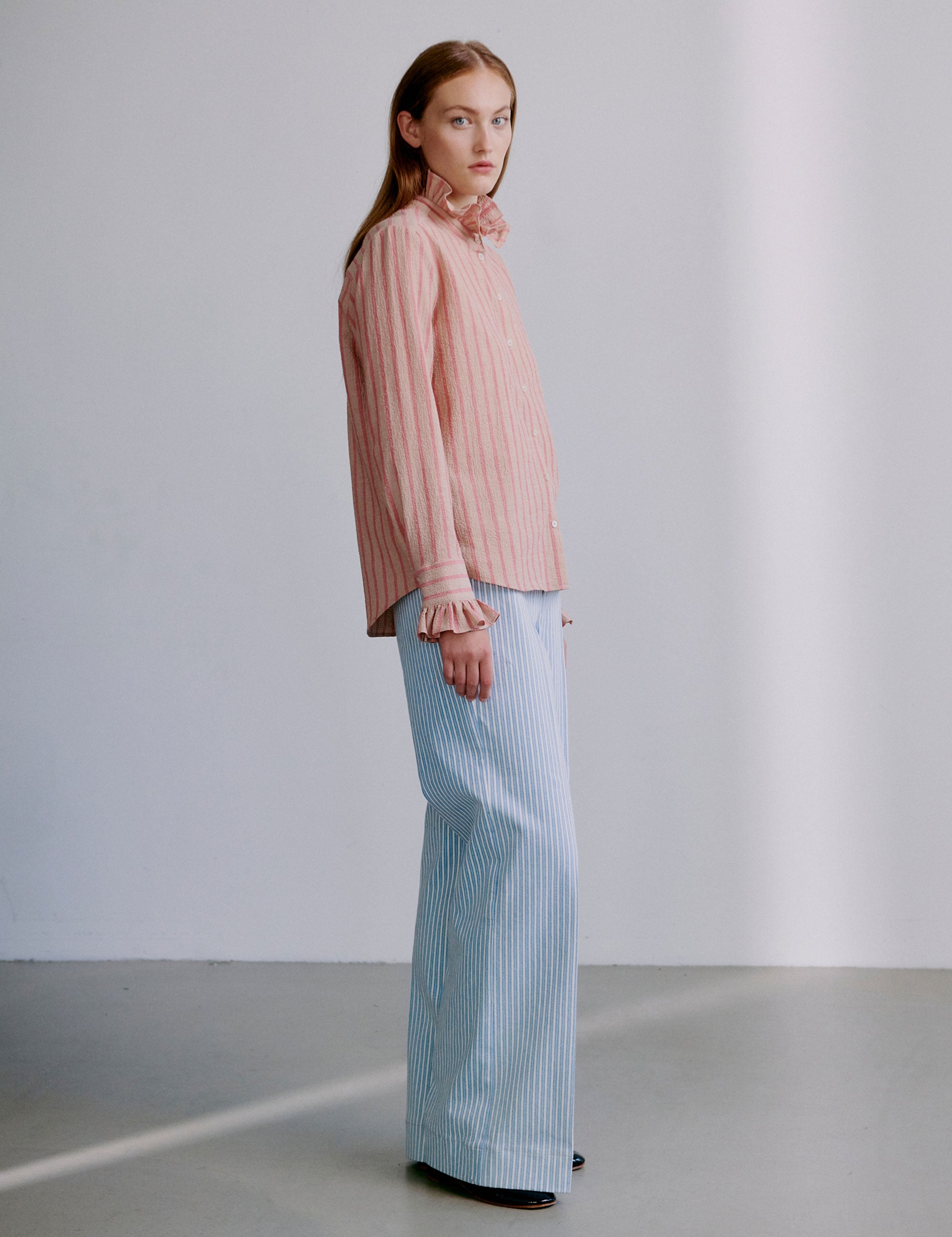 Woman wearing a pink and red striped seersucker shirt with ruffled sleeves and collar and light blue and white striped pants