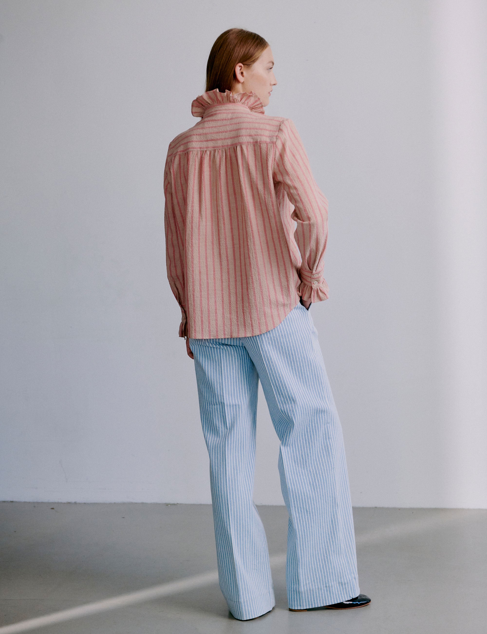 Woman wearing a pink and red striped seersucker shirt with ruffled sleeves and collar and light blue and white striped pants