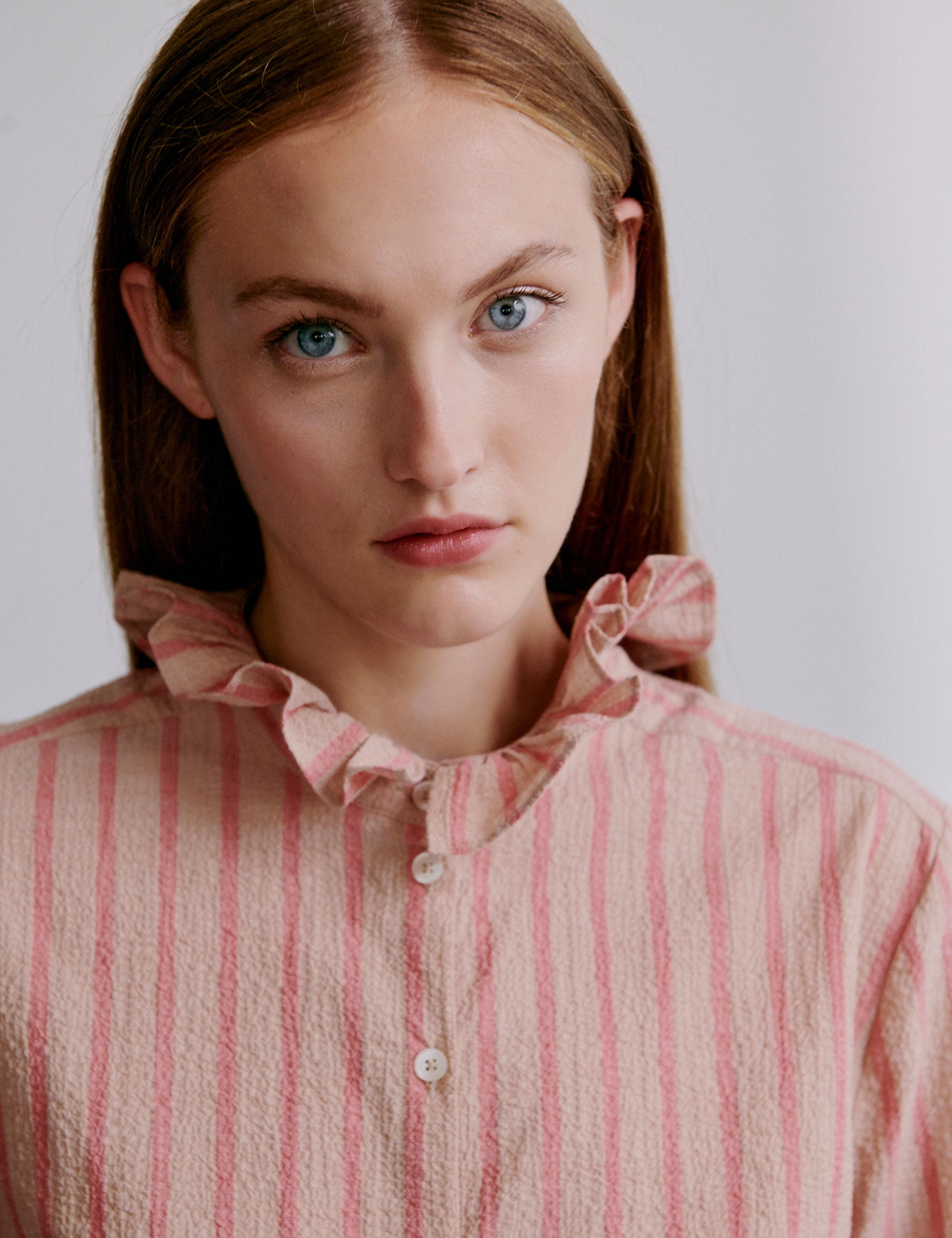 Woman wearing a pink striped shirt with a ruffled collar and buttons
