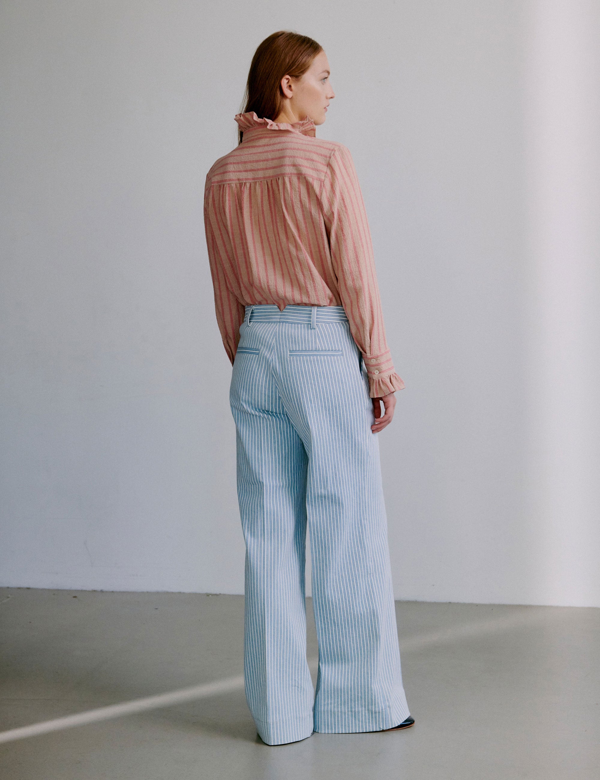 Woman wearing a pink and red striped seersucker shirt with ruffled sleeves and collar and light blue and white striped pants