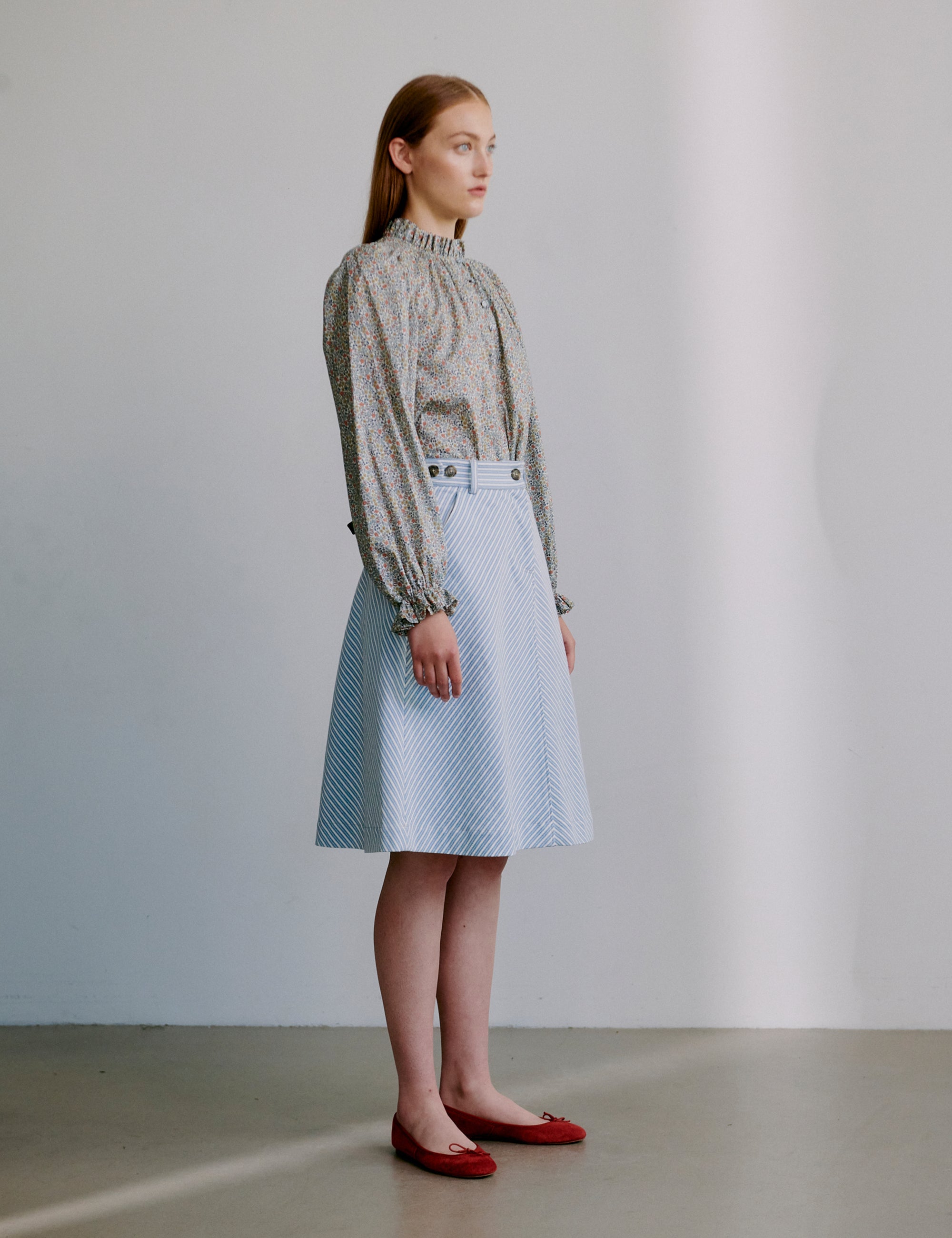 Woman wearing a floral patterned blouse and light blue skirt with red shoes 