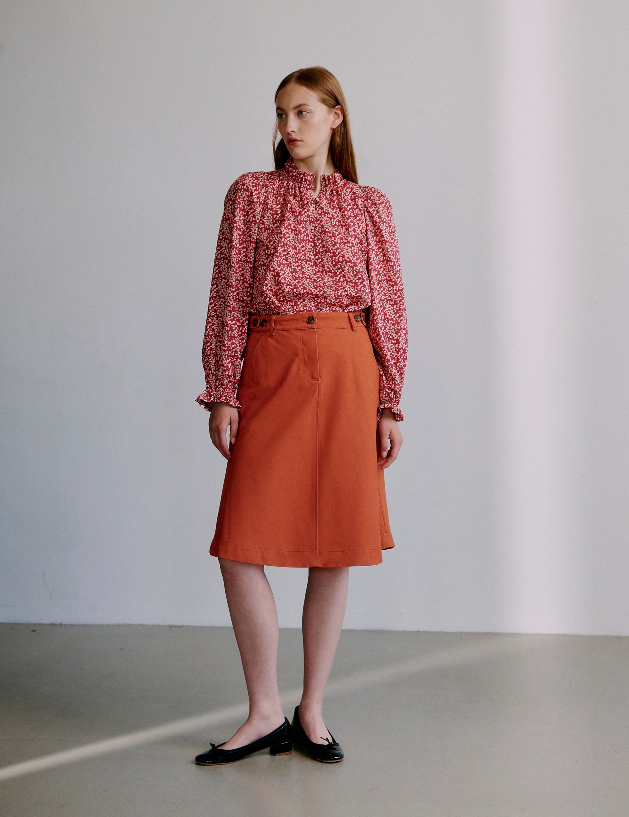 Woman wearing a red floral blouse and orange skirt against a plain background