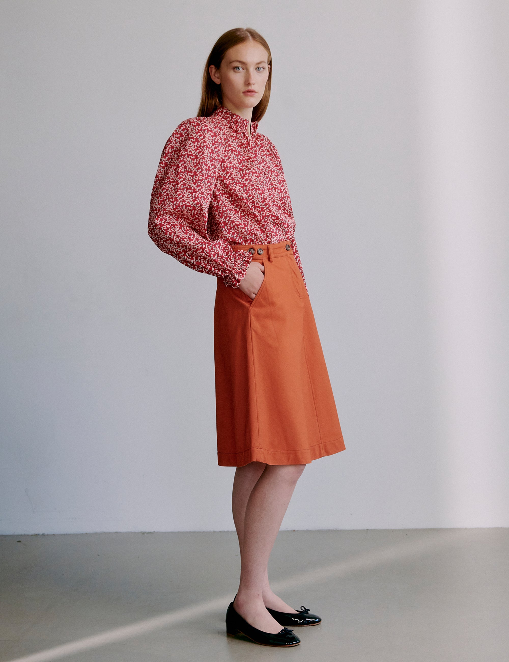 Woman wearing a red floral blouse and orange a-line skirt and black shoes