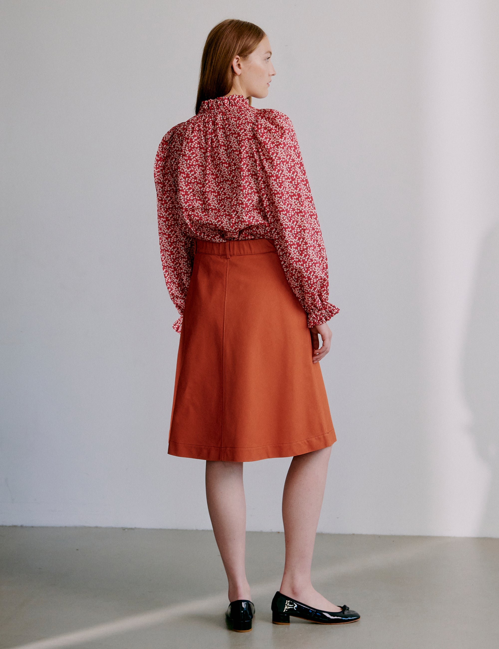 Woman wearing a red floral blouse and orange a-line skirt and black shoes