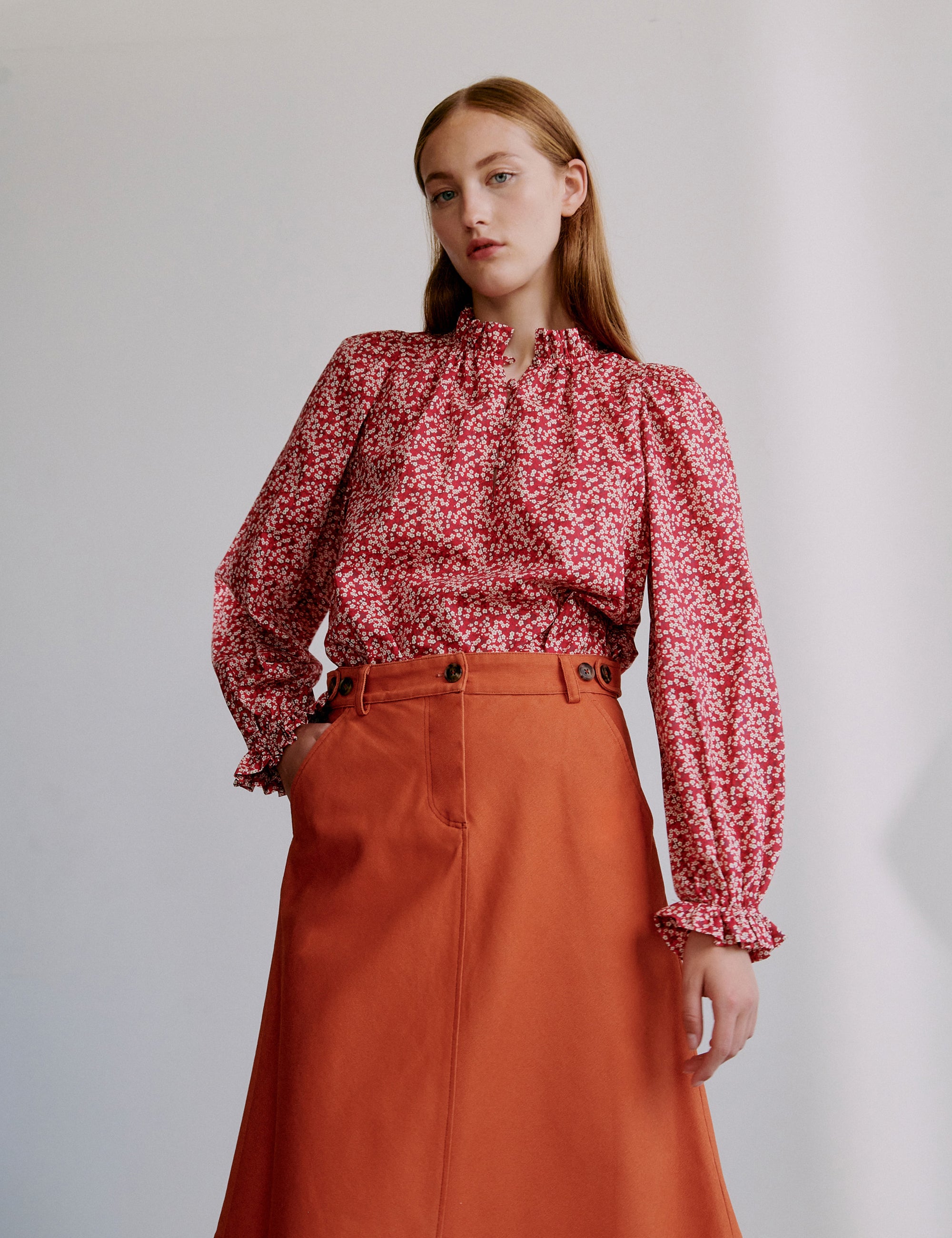 Woman wearing a red floral blouse and orange a-line skirt with pockets