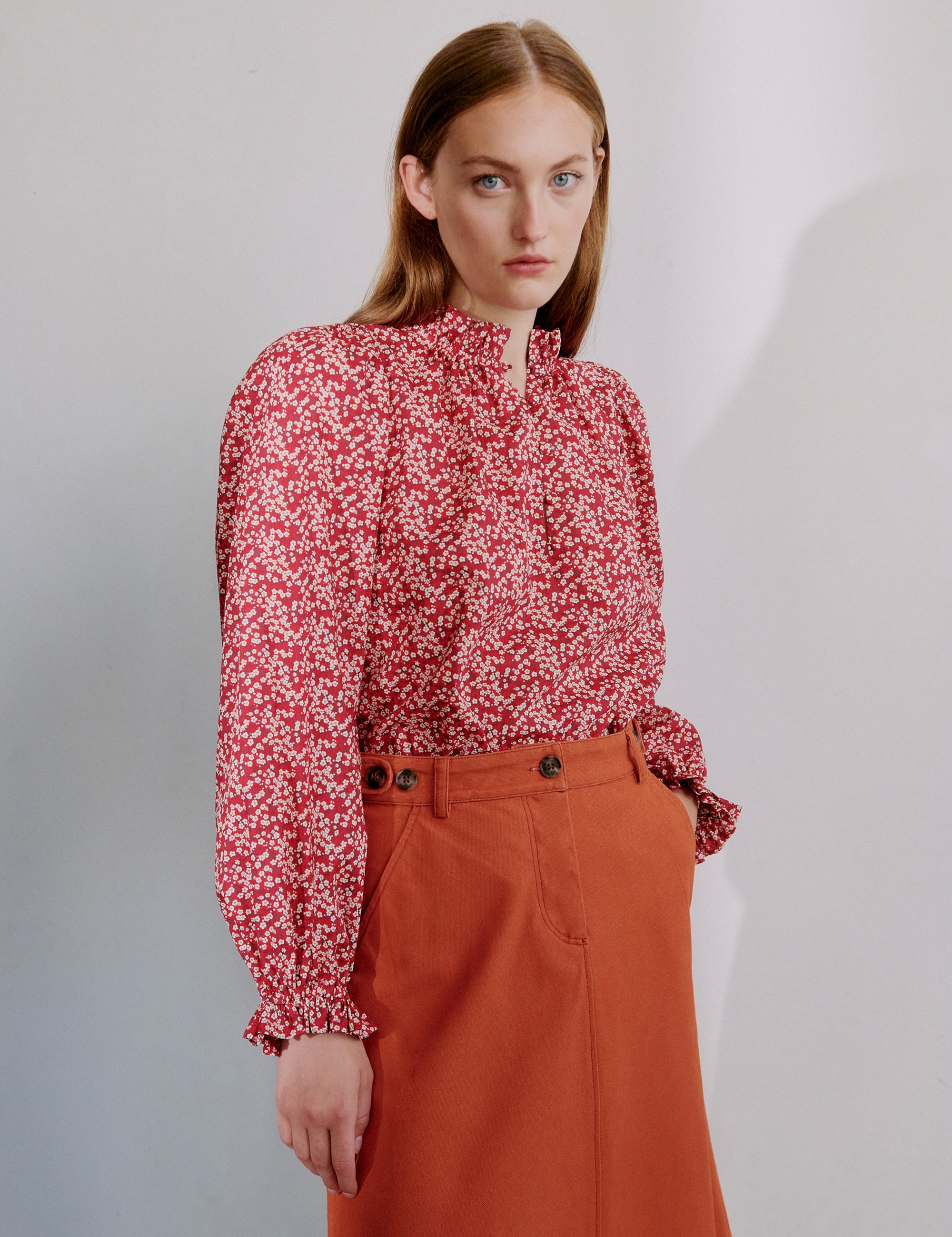 Woman wearing a red floral blouse and orange a-line skirt with pockets